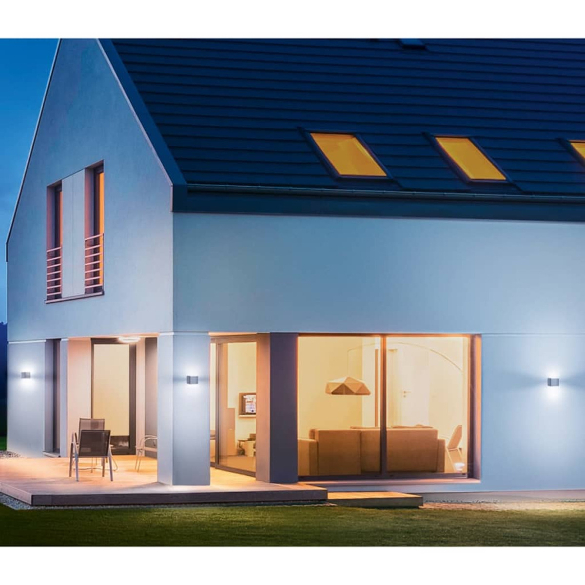 Ein zweistöckiges Haus mit großen Fenstern, einem dunklen Dach und einem gut beleuchteten Innenraum, mit Rasen im Vordergrund.