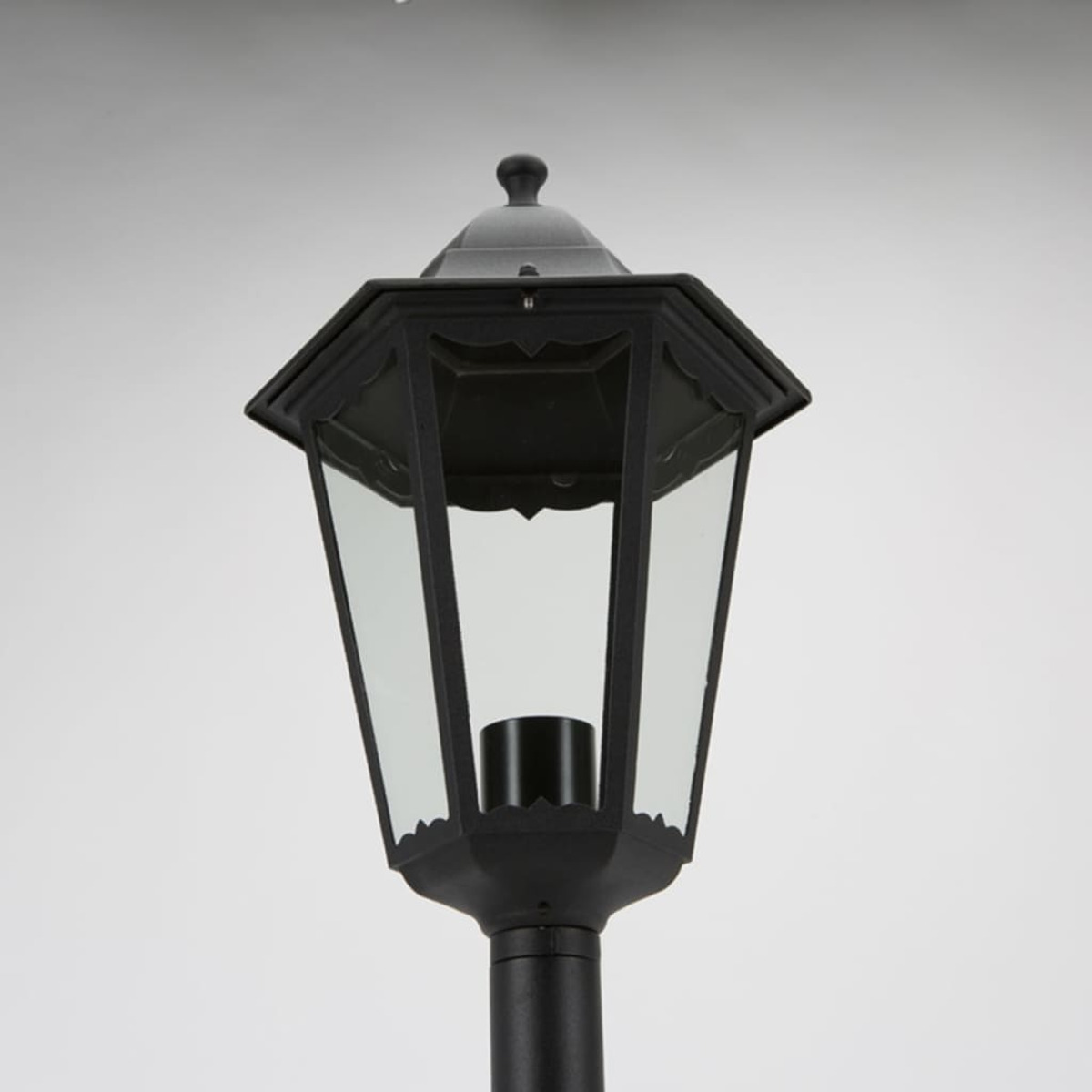 Una lampada da esterno nera con un tetto esagonale e pannelli di vetro trasparente.