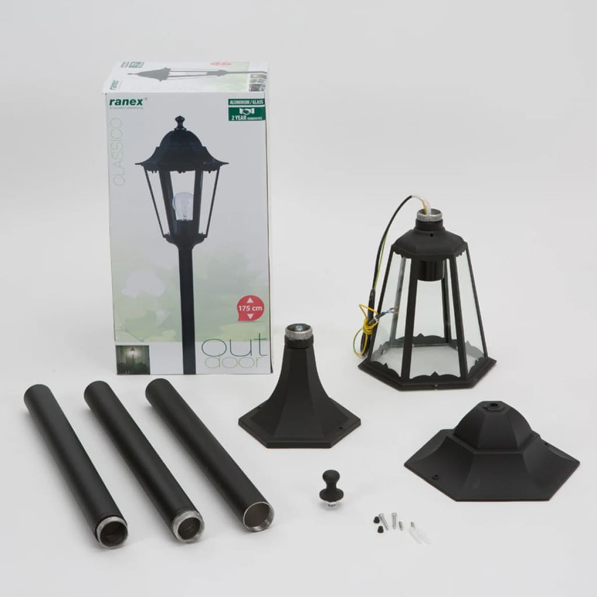 Componenti di lampada da esterno, in scatola, con base, testa della lampada, pali e viti, su sfondo bianco.