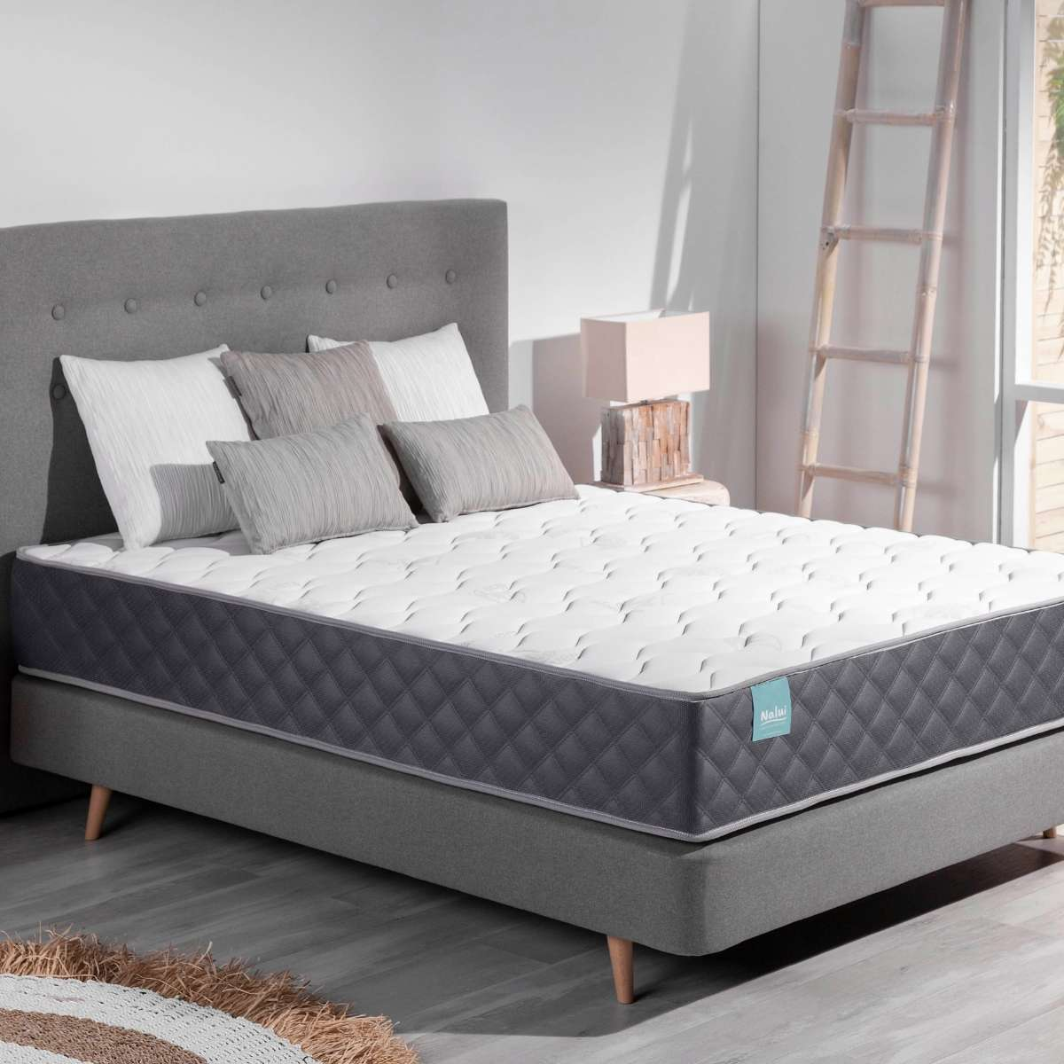 Una cama con cabecero gris y colchón blanco.