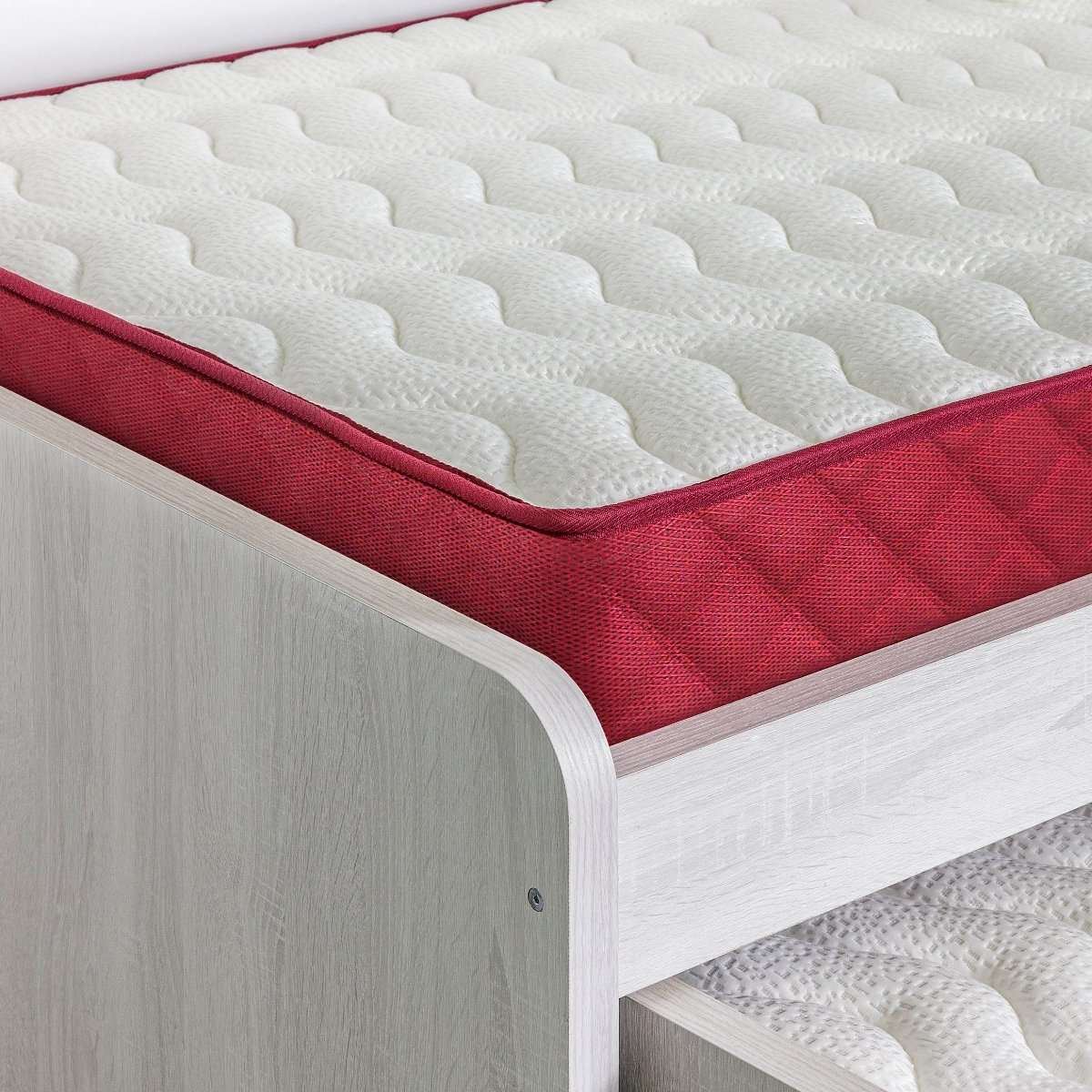 Primer plano de una cama con colchón blanco con borde rojo, sobre un marco de madera.