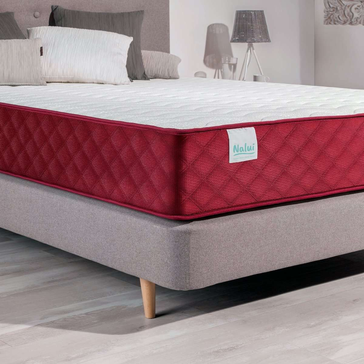 Una cama con un colchón superior blanco y un lateral rojo, sobre una base gris, con almohadas.