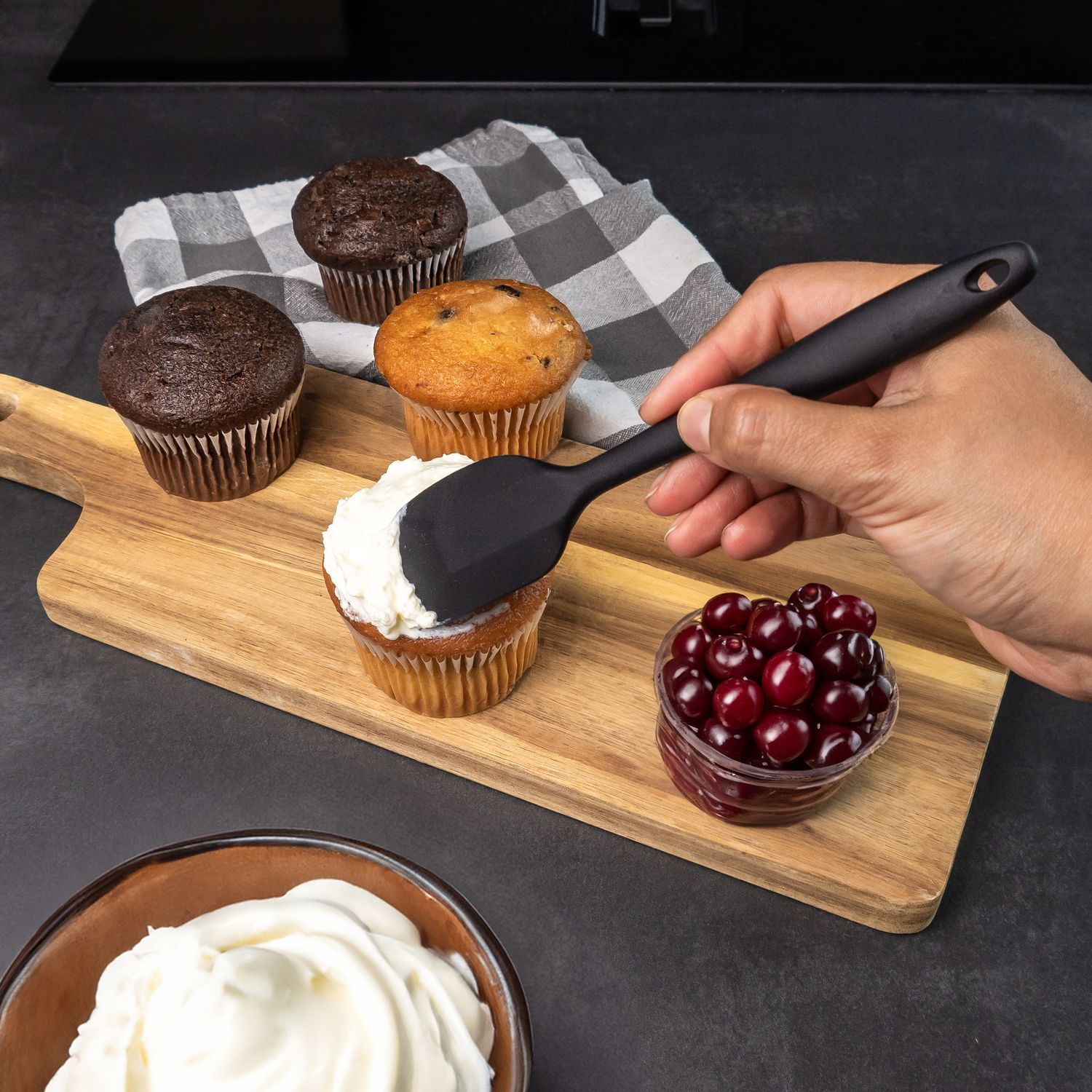 Eine Person, die einen Cupcake mit Zuckerguss und Kirschen auf einem Holzbrett dekoriert.