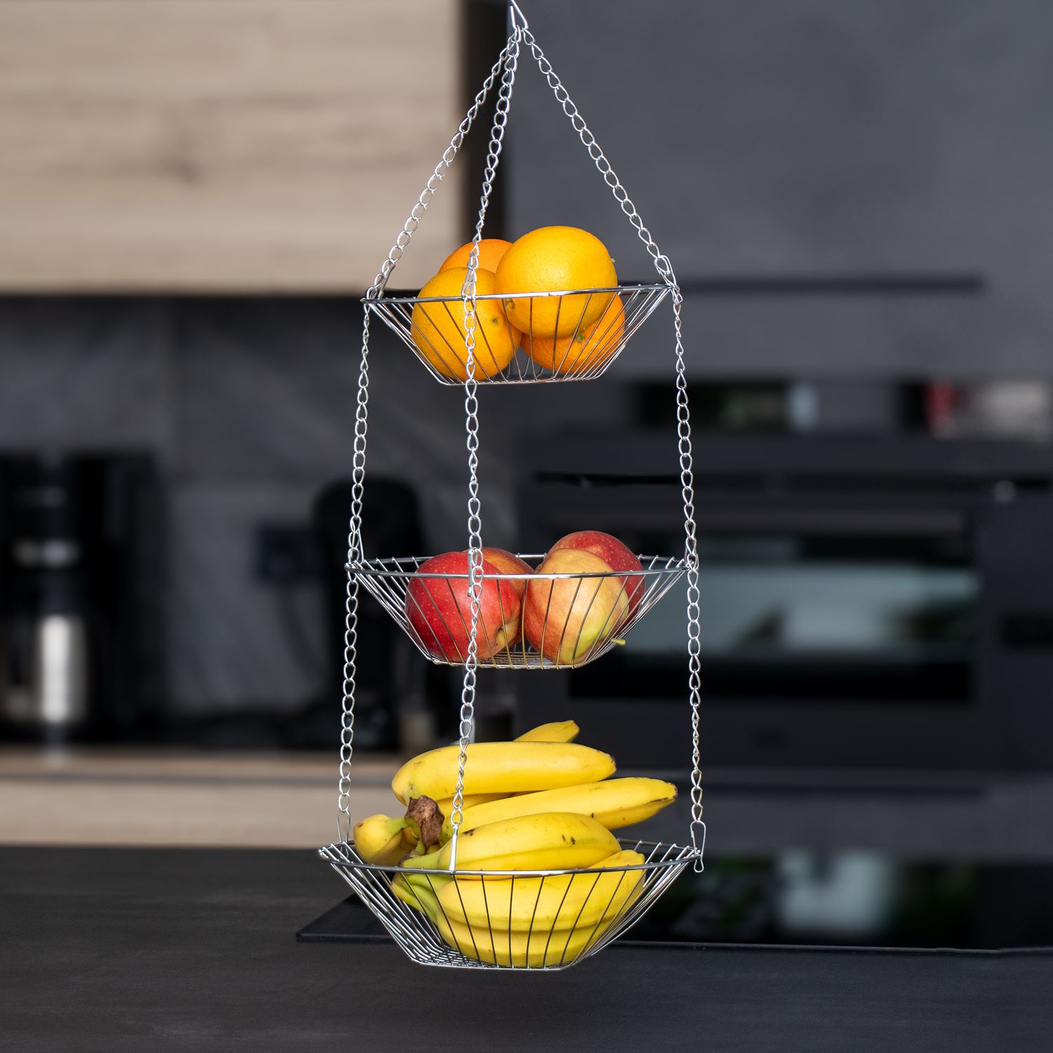 Hänge-Obstkorb mit Orangen, Äpfeln und Bananen auf dunklem Hintergrund.
