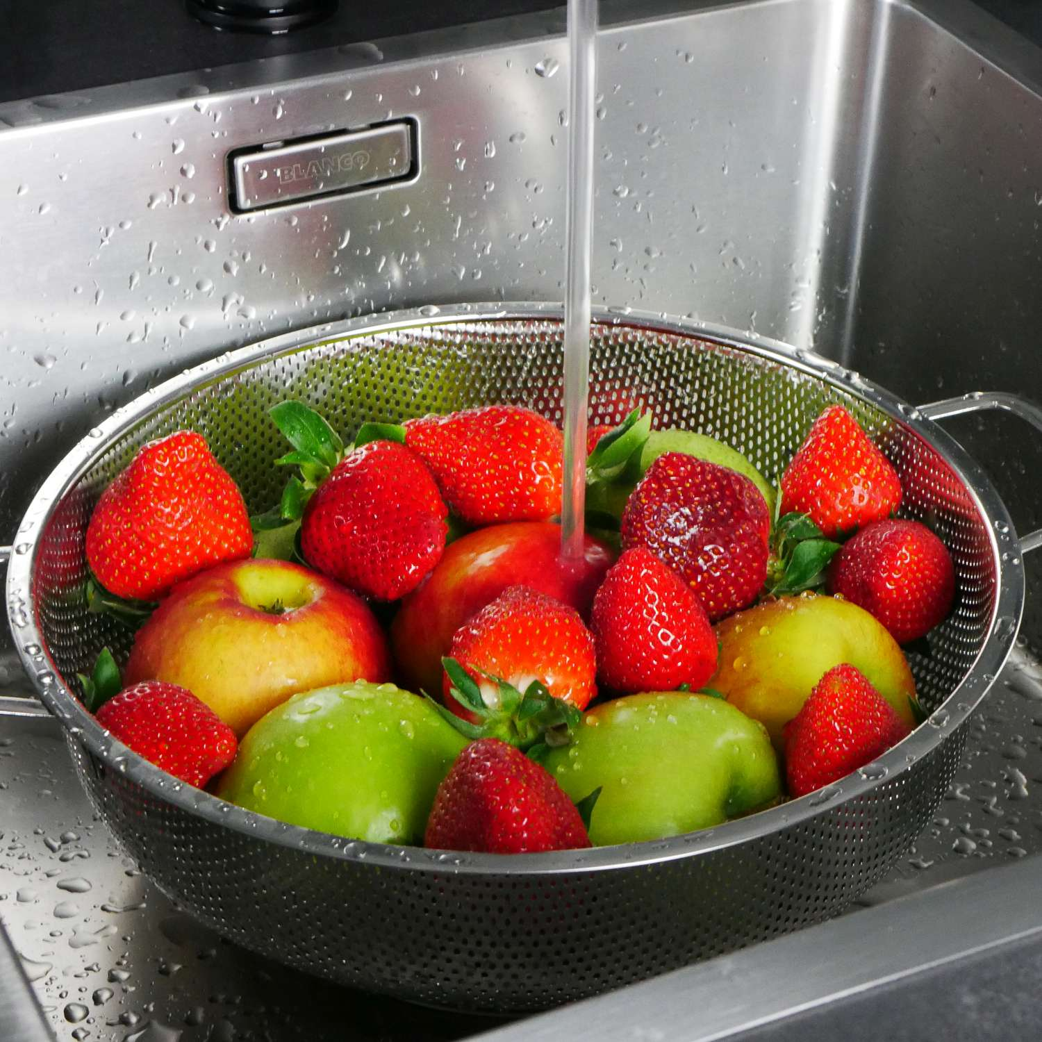 Erdbeeren, Äpfel und Wasser in einem Metall-Sieb in einem Küchenbecken.