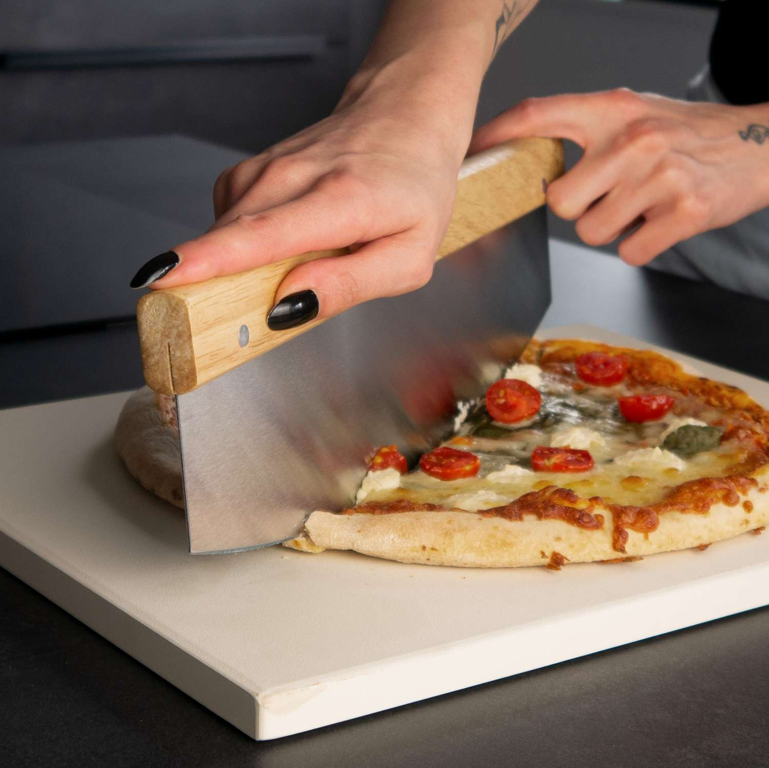 Person schneidet Pizza auf weißem Brett mit Holz-Metall-Schneider.
