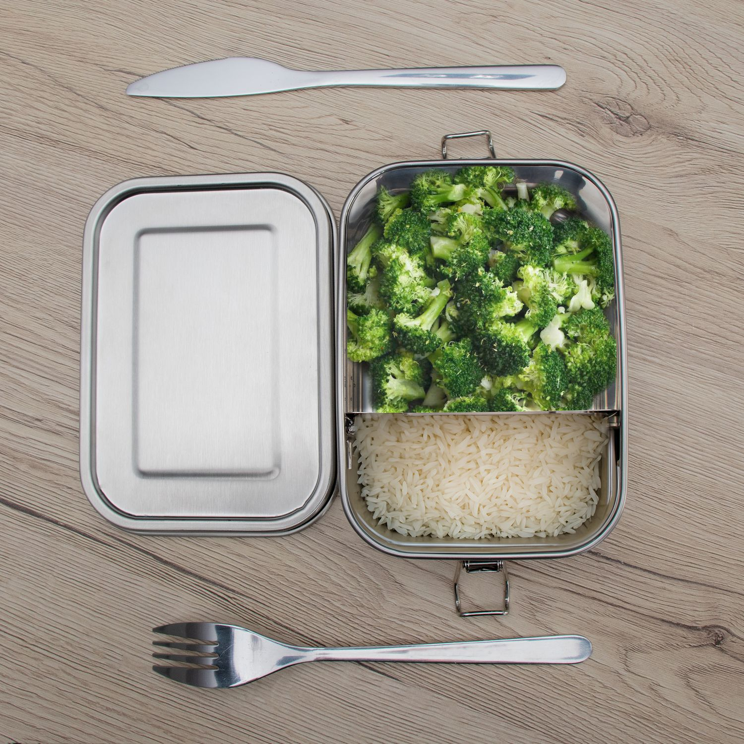Lunchbox mit Brokkoli und Reis, Gabel und Messer auf einem Holztisch.