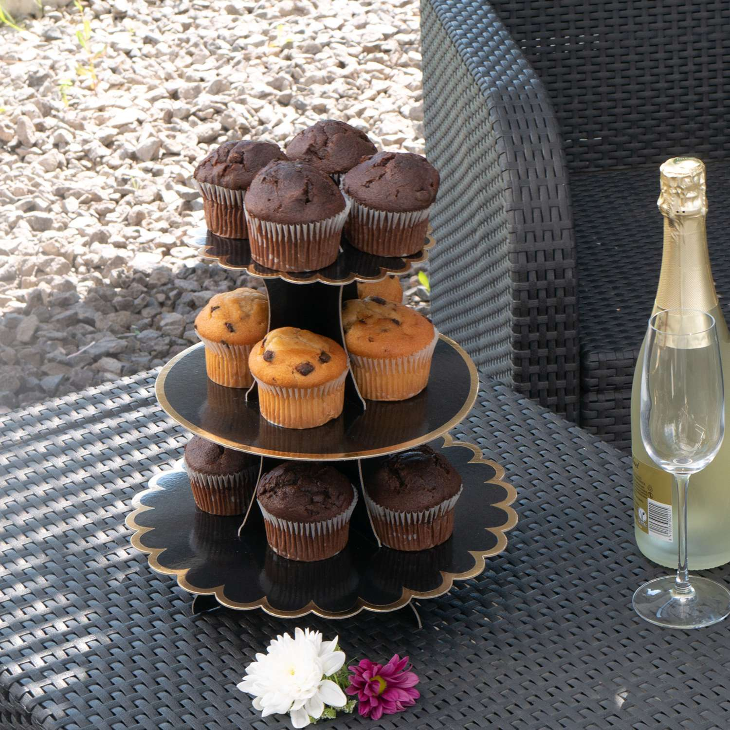 Ein mehrstöckiger Cupcake-Ständer mit Cupcakes, eine Flasche und ein Glas auf einem Tisch.