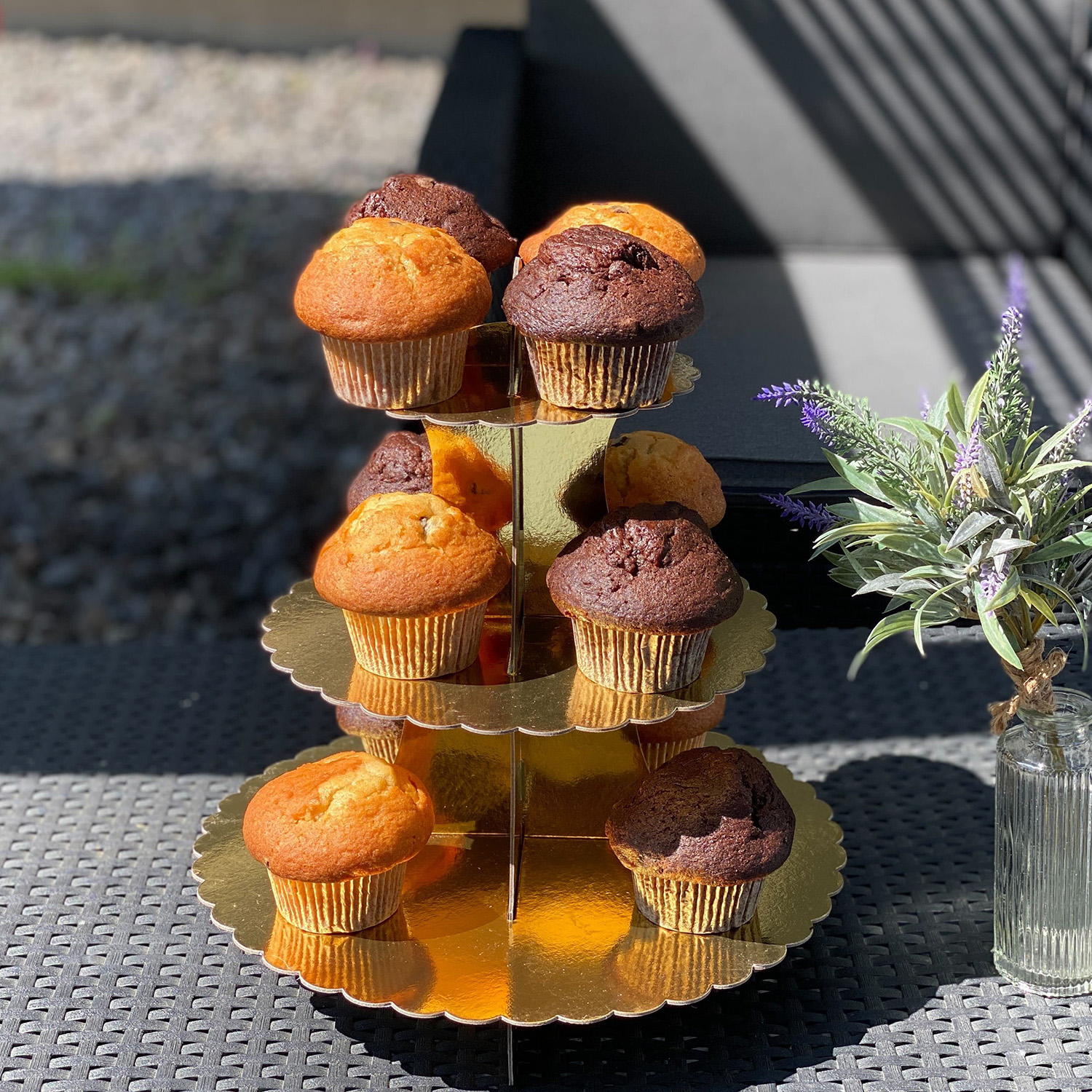 Ein dreistöckiger goldener Ständer mit mehreren Muffins, mit einem Blumenstrauß im Hintergrund.