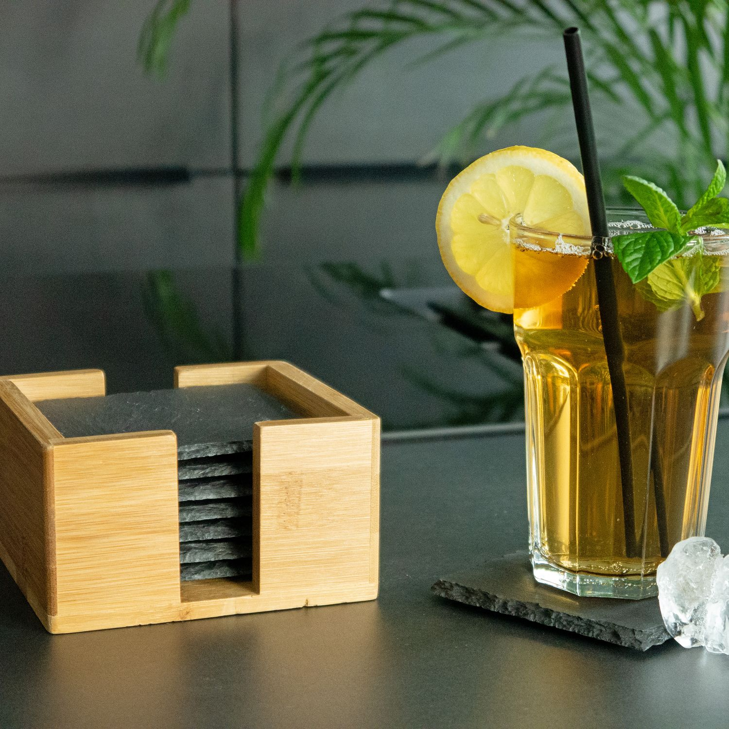 Glas Eistee mit Zitrone, Minze und Strohhalm, plus Untersetzer in Holzhalter.