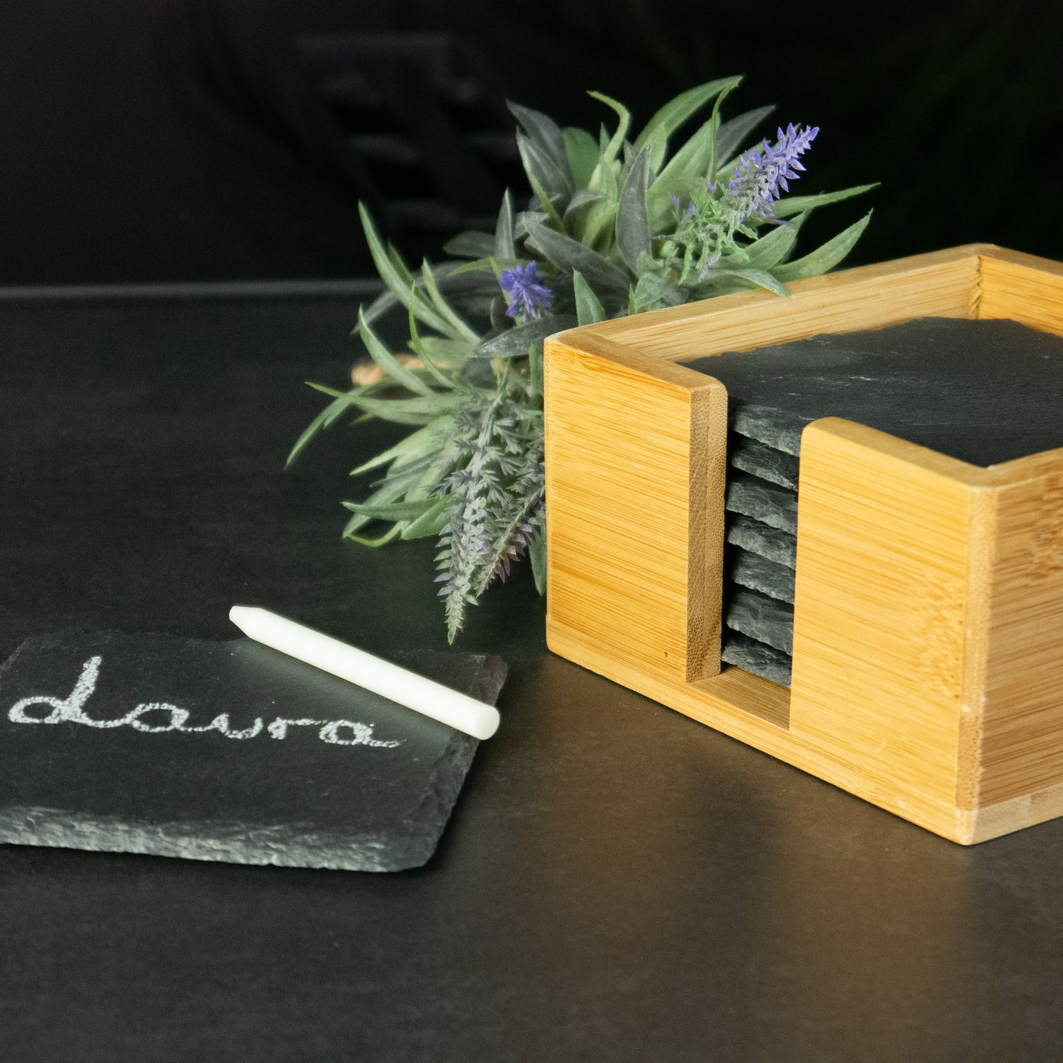 Ein hölzerner Untersetzerhalter mit Untersetzern und ein mit Kreide beschriftetes Namensschild. Lavendel und Laubwerk sind im Hintergrund.