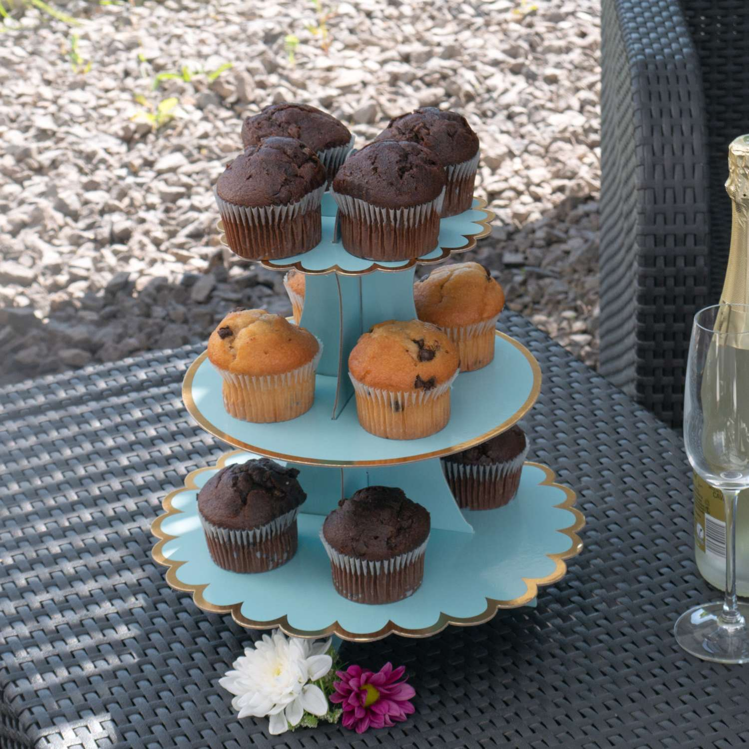 Ein dreistöckiger Cupcake-Ständer mit Cupcakes. Es gibt eine Flasche Champagner und eine Blume.