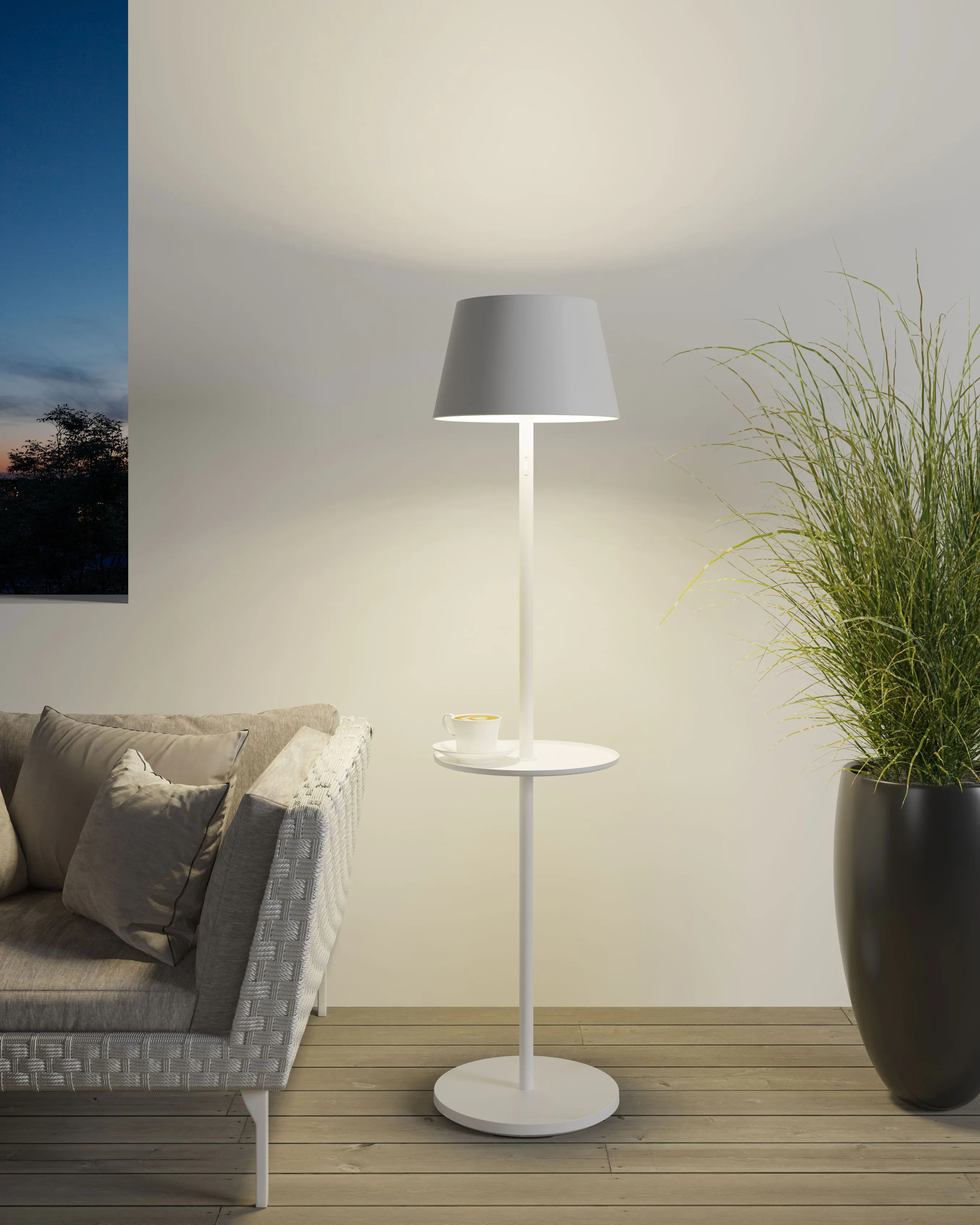 Lampada da terra bianca con tavolino, tazza e pianta alta, su sfondo scuro.