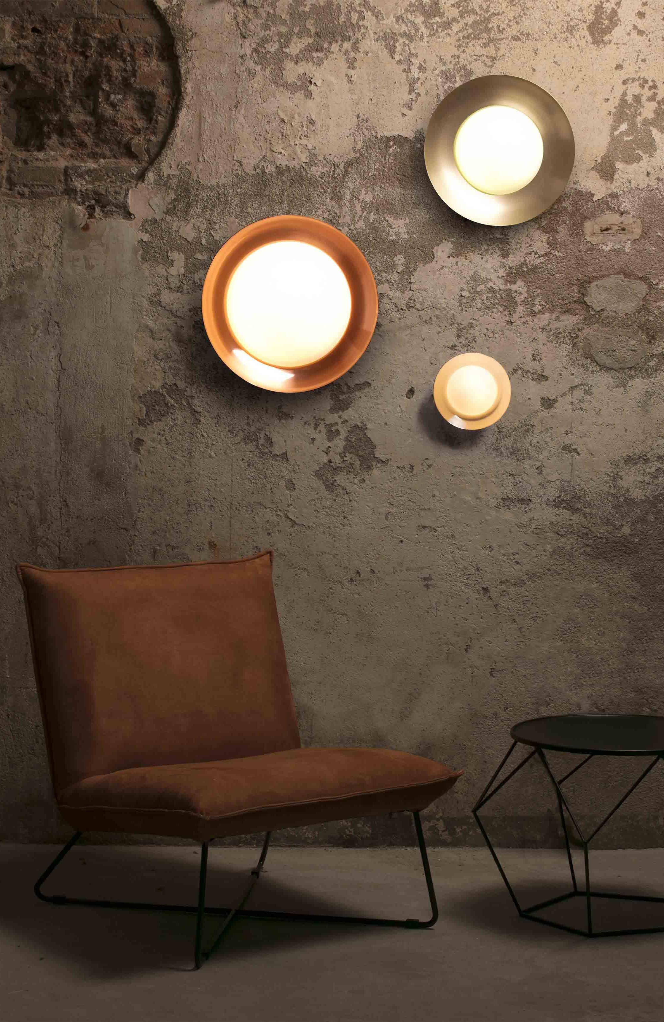 Tre luci circolari su un muro strutturato. Una sedia e un tavolino in primo piano.