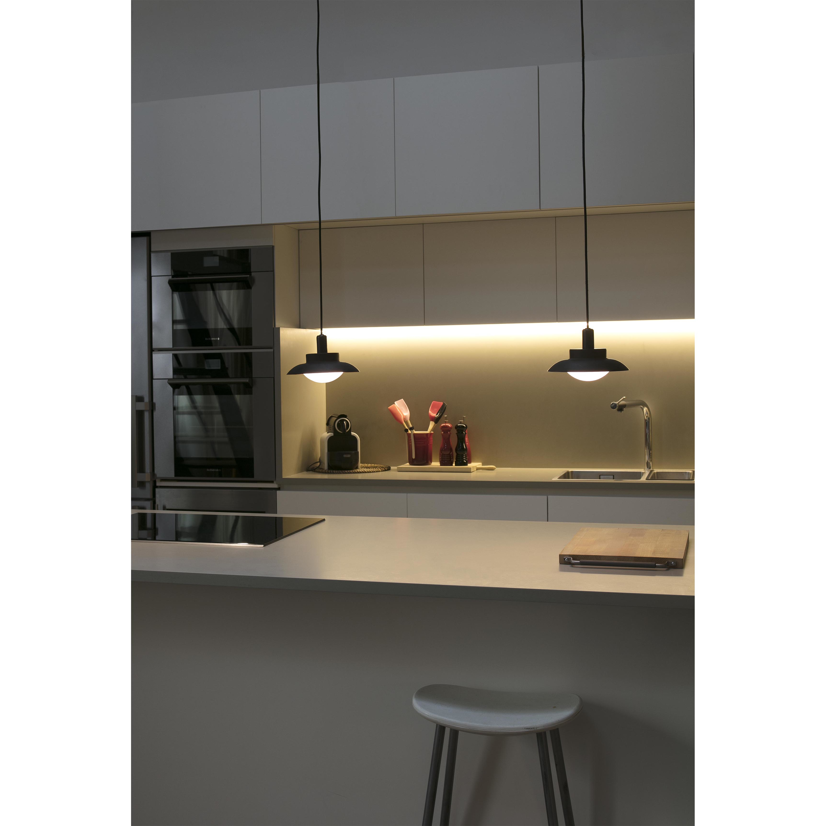 Cucina moderna con due lampade a sospensione, piano chiaro e sgabello.