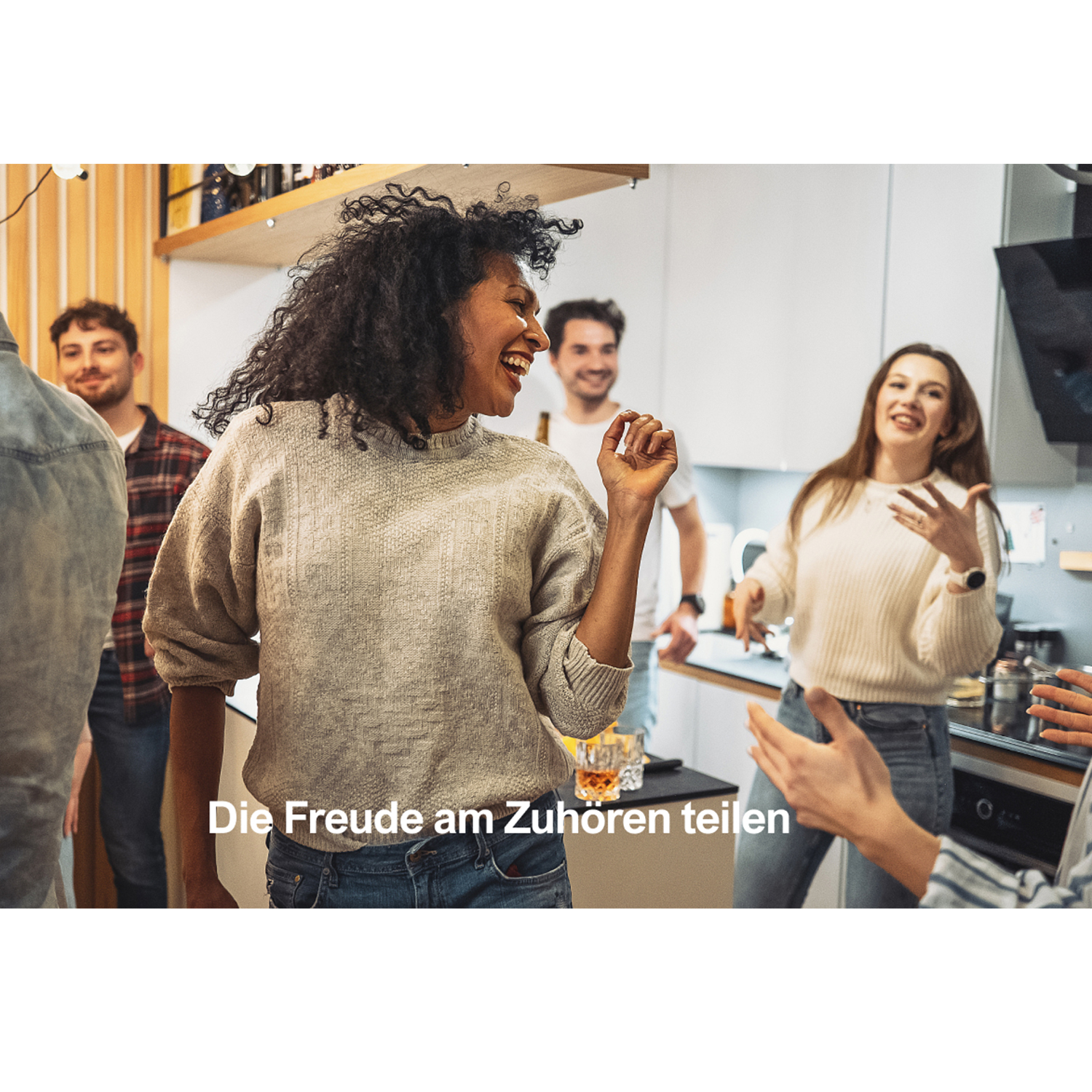 Menschen lachen in einer Küche. Eine Frau tanzt. Andere sind im Hintergrund.