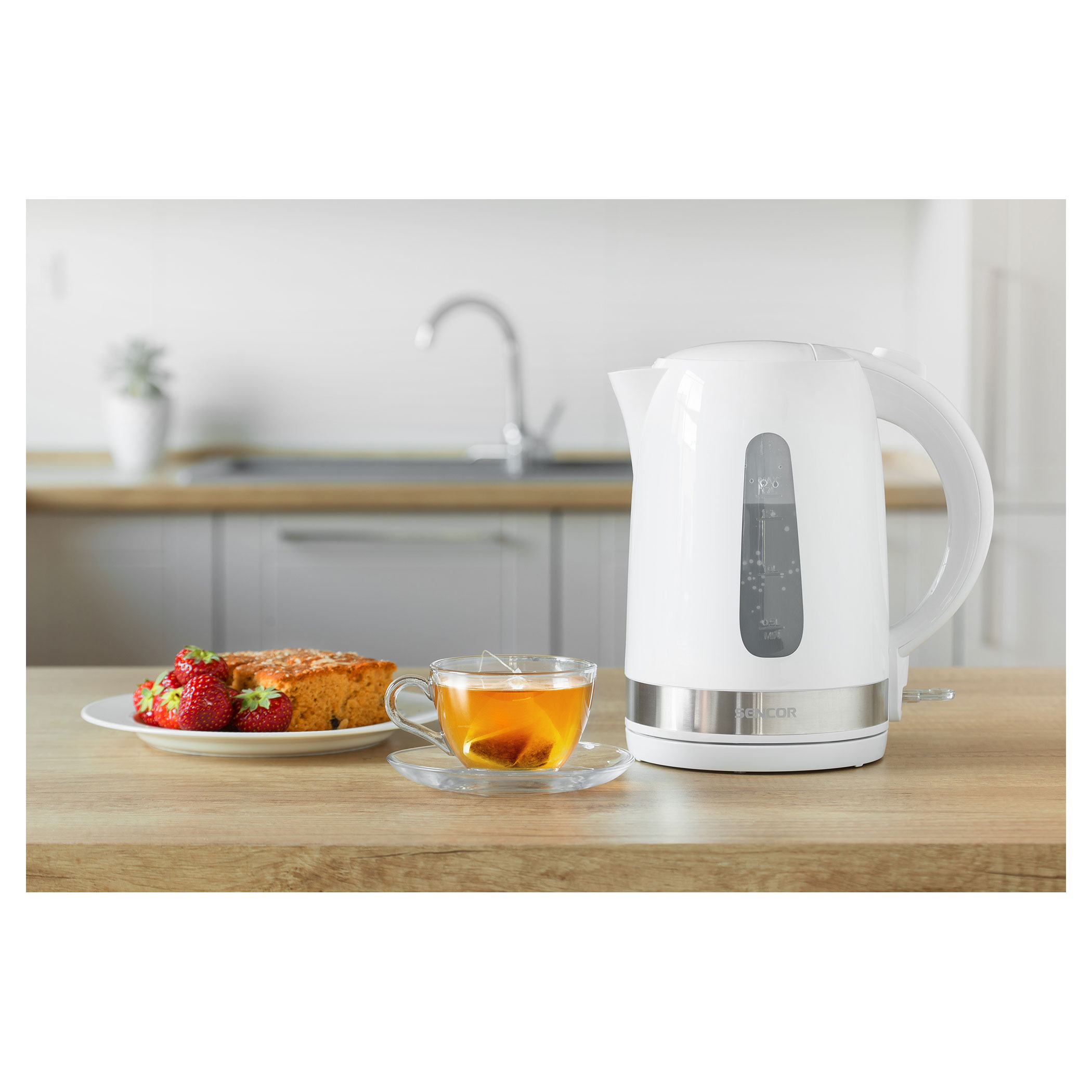 Scena cucina con bollitore bianco, tè, torta e fragole su un tavolo.