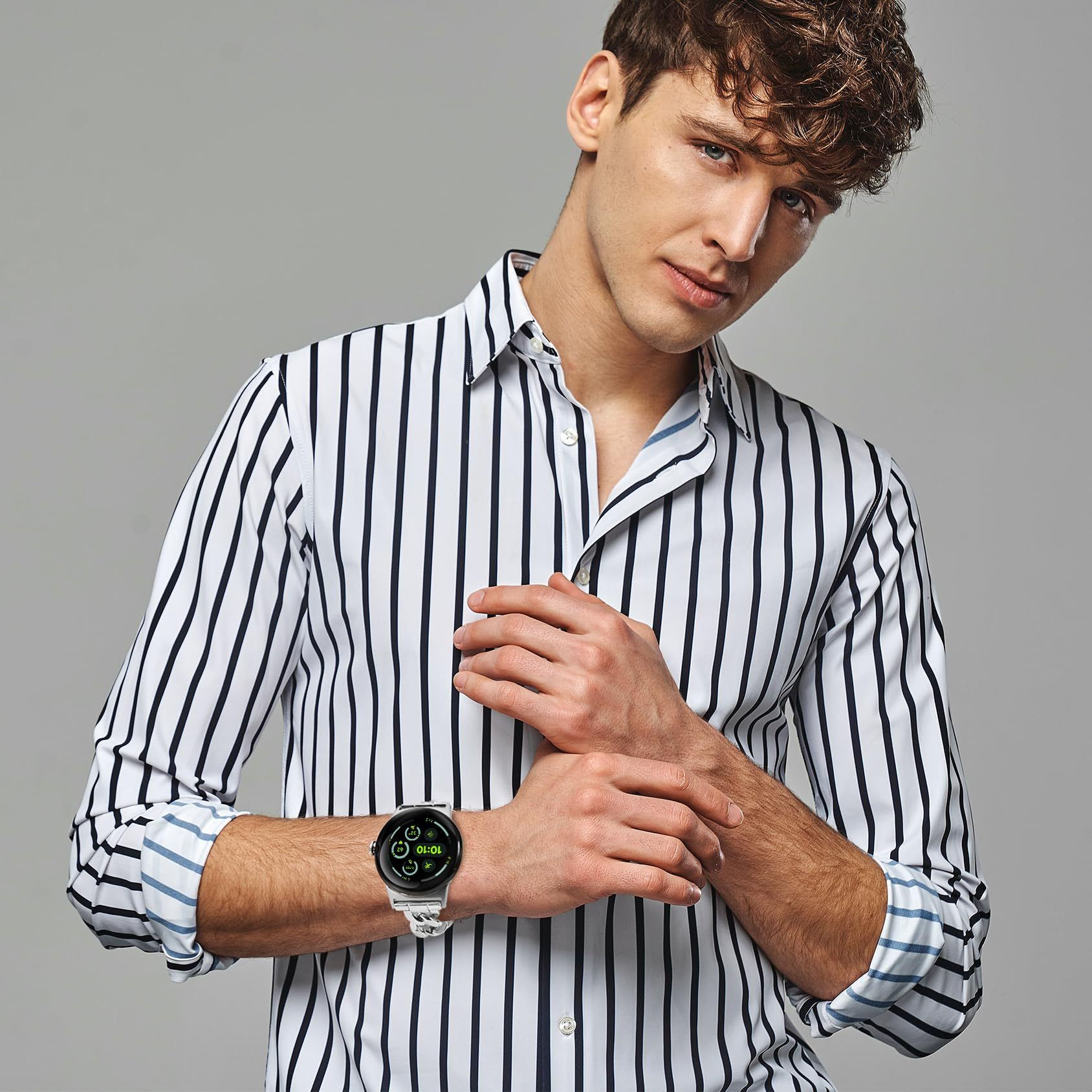 Un uomo con camicia a righe e smartwatch, guarda verso la fotocamera, sfondo grigio.