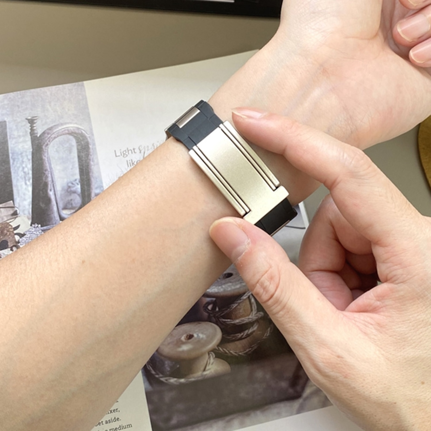 Hand mit Smartwatch mit Metallband über einem Buch.