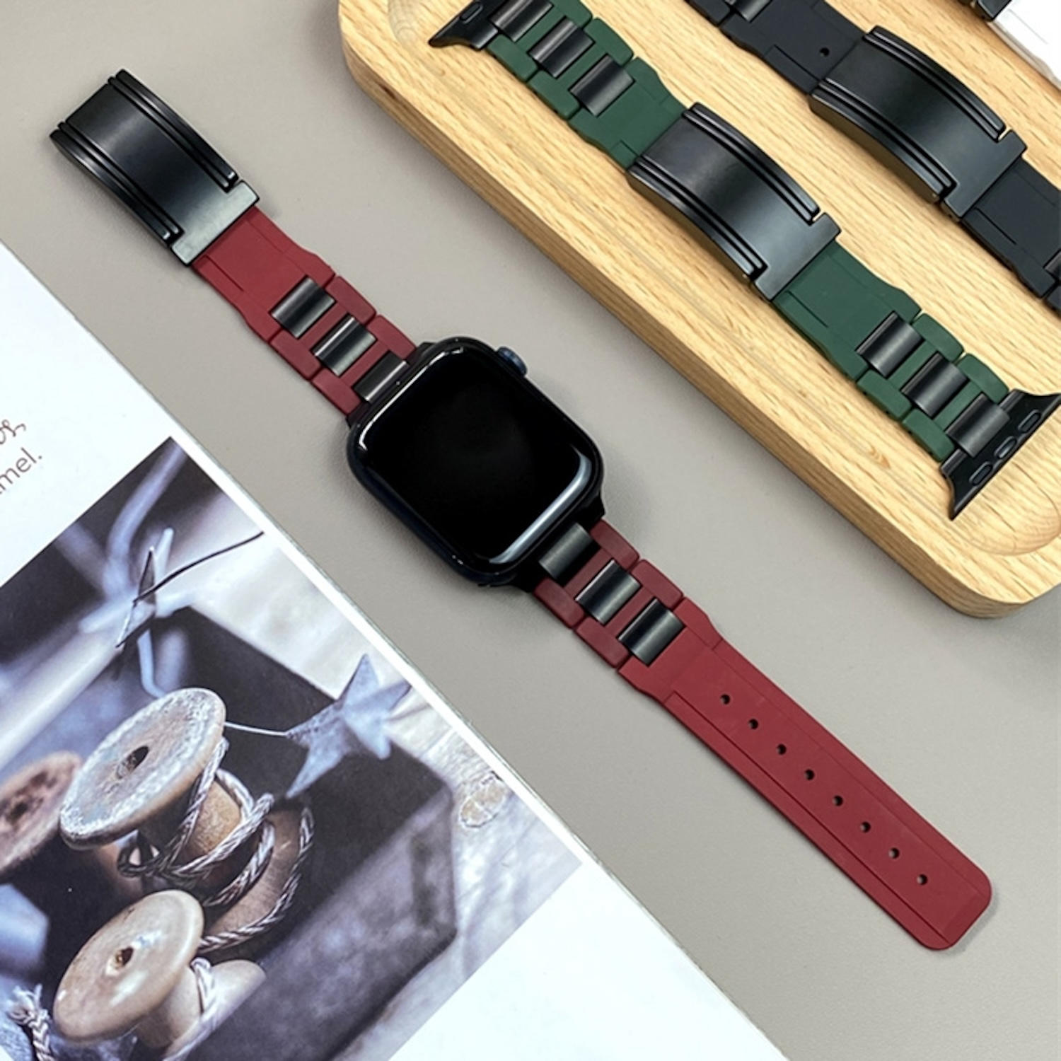 Apple Watch mit rotem Armband und zwei weiteren Bändern auf Holzoberfläche.