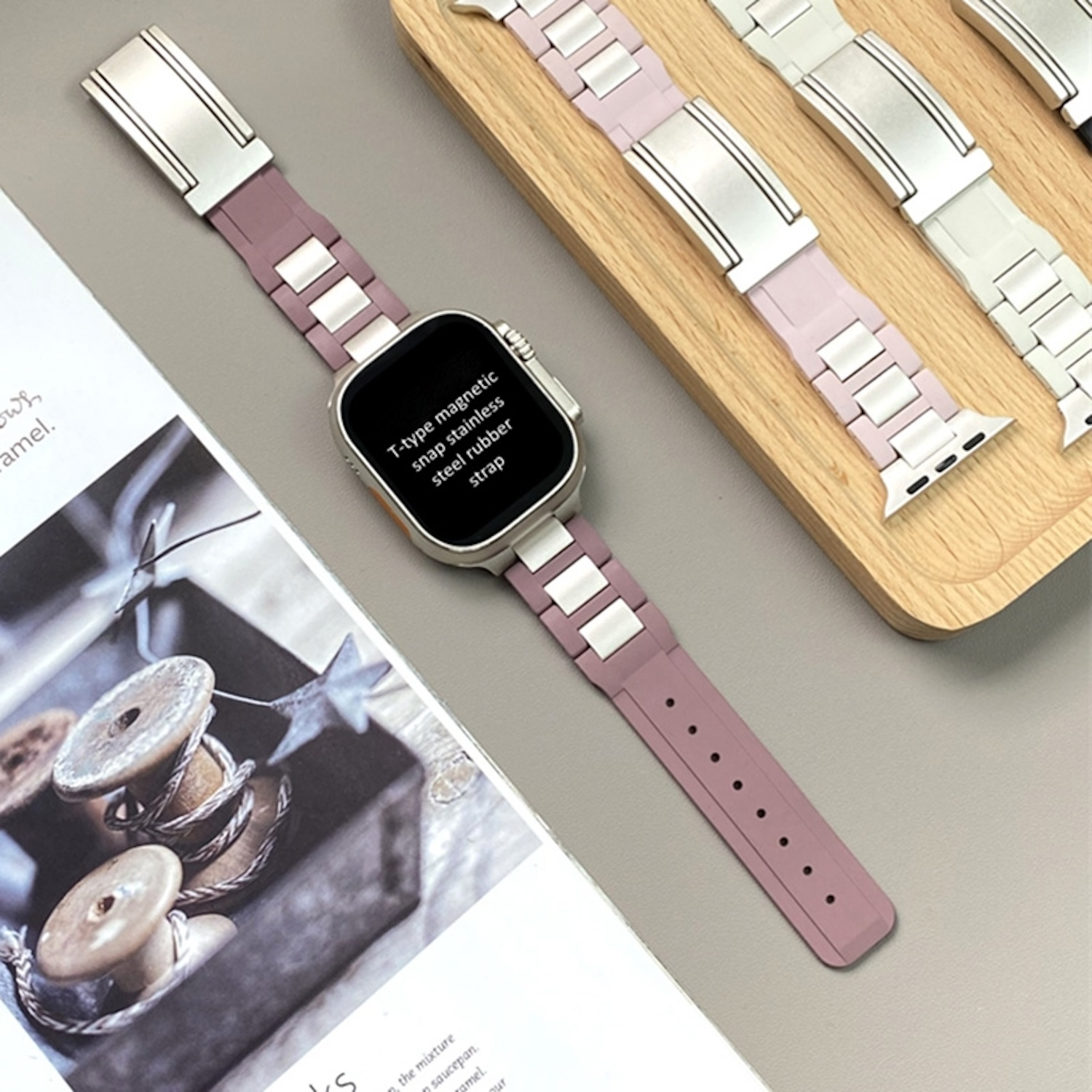 Eine Uhr mit pinkfarbenem Armband und silberfarbenen Akzenten auf einem Holztablett. Andere Armbänder sind sichtbar.