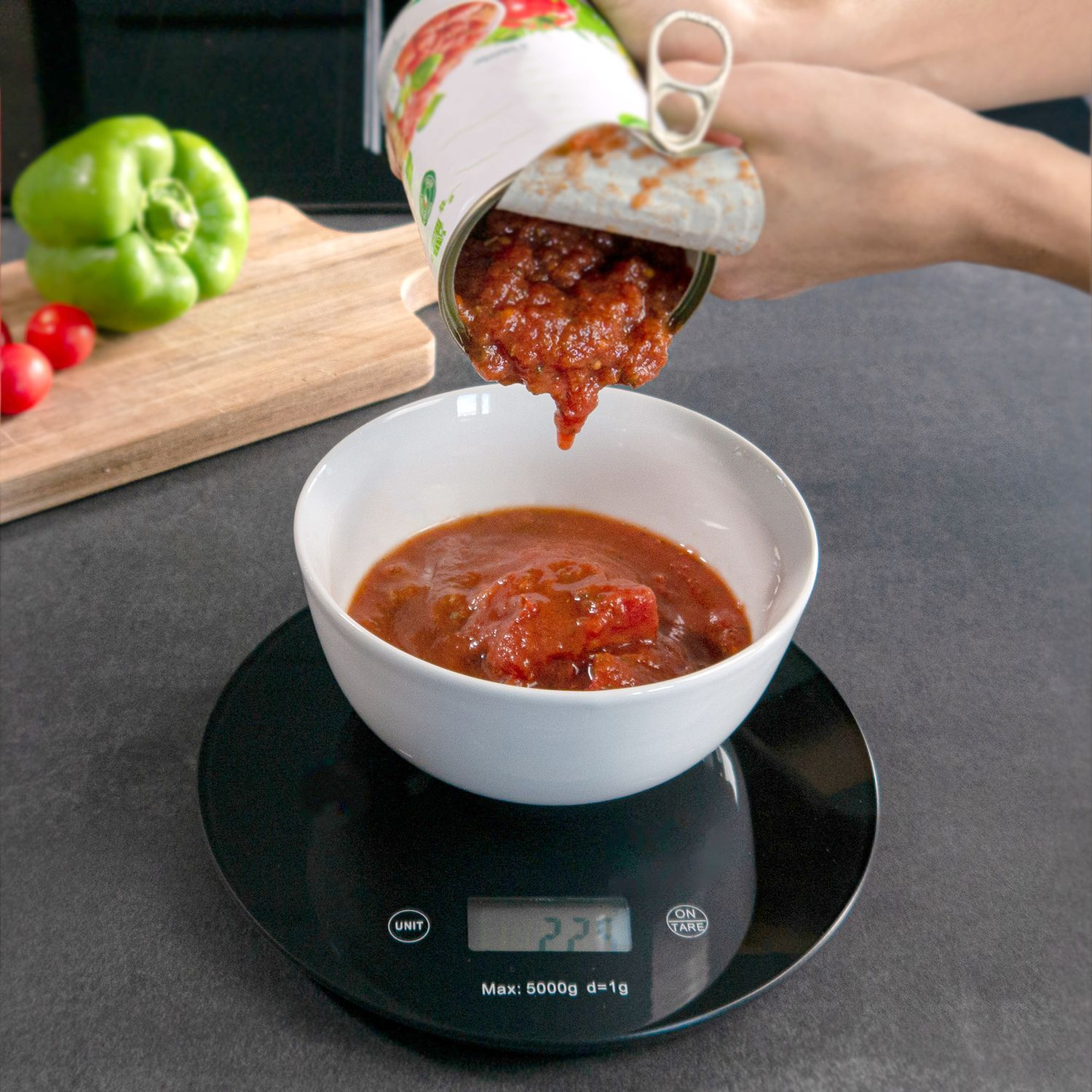 Eine Dose Tomatensauce, die in eine weiße Schüssel auf einer Waage gegossen wird.