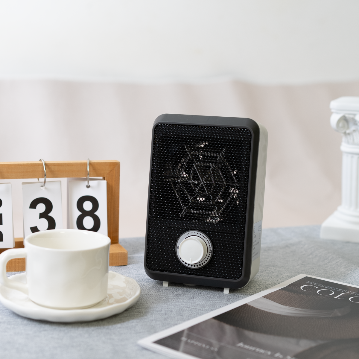 Un pequeño calefactor eléctrico blanco sobre una mesa. Un calendario y una revista cerca.