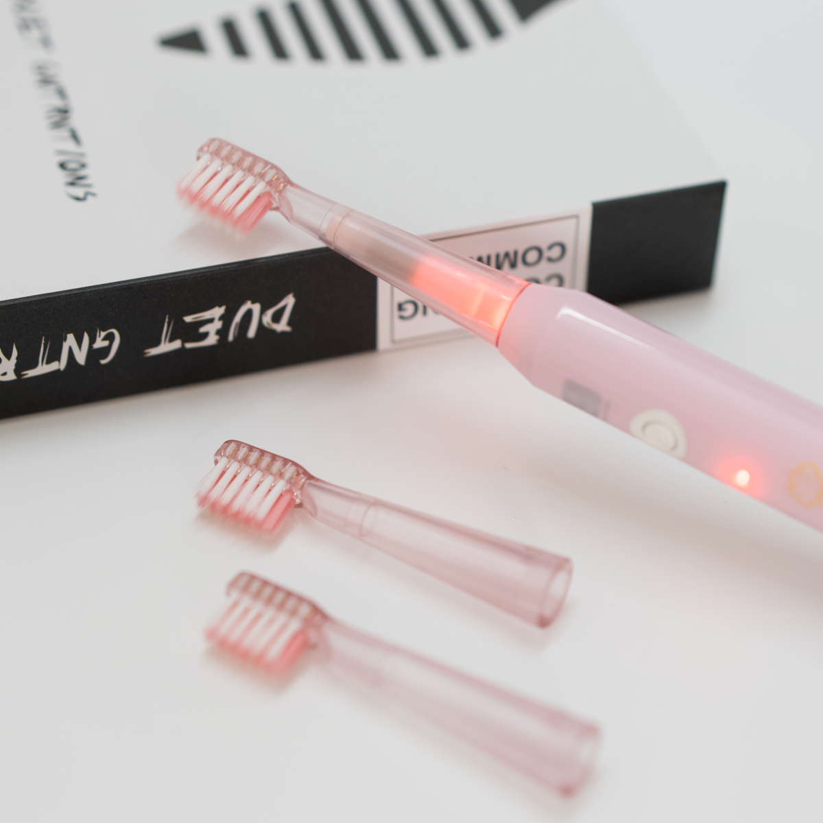Cepillo de dientes eléctrico rosa con dos cabezales de repuesto y un libro detrás.