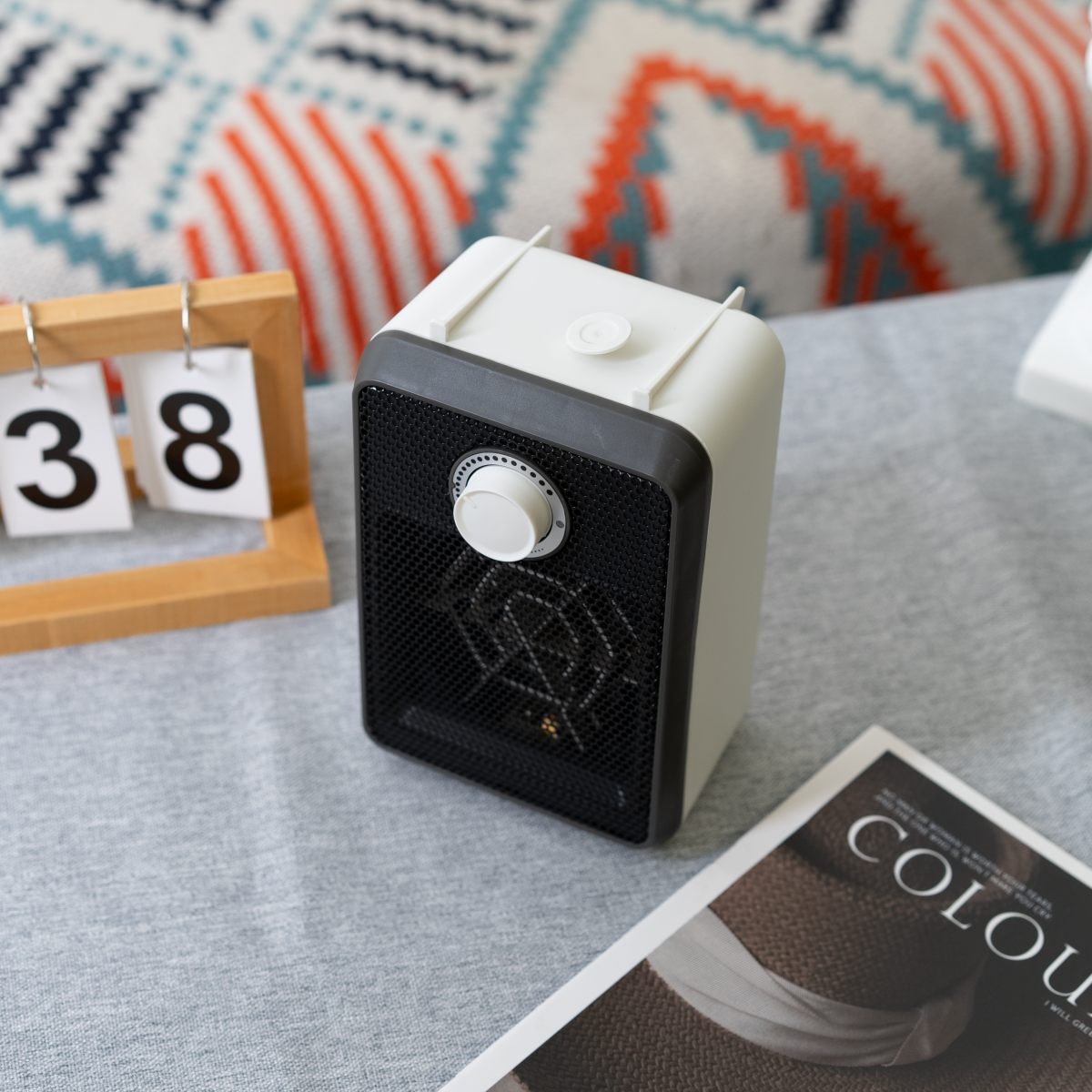 Un calefactor blanco y gris con una perilla, sobre una superficie gris con una revista y calendario.
