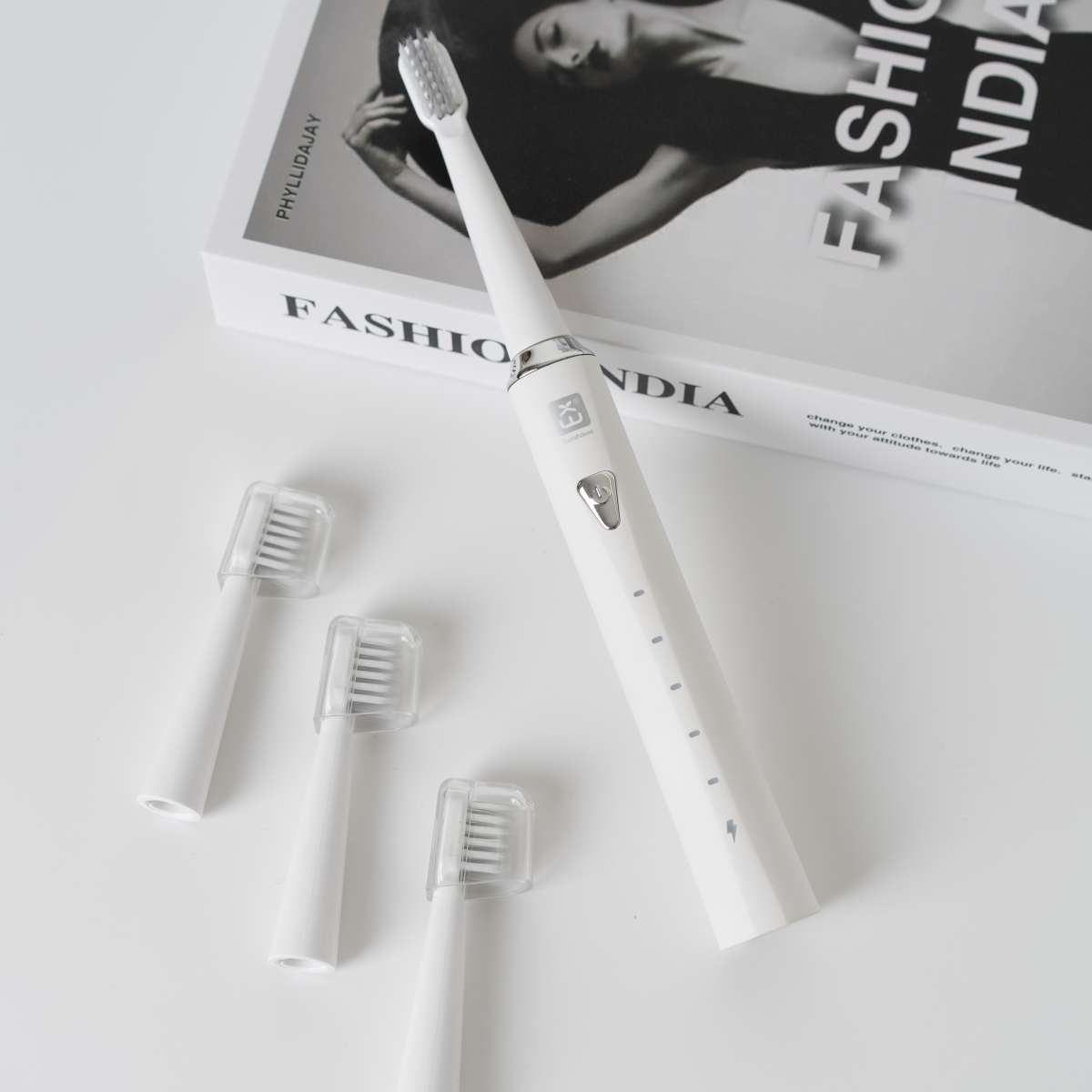 Cepillo de dientes eléctrico blanco con cabezales de repuesto y libro 'Fashion India'.