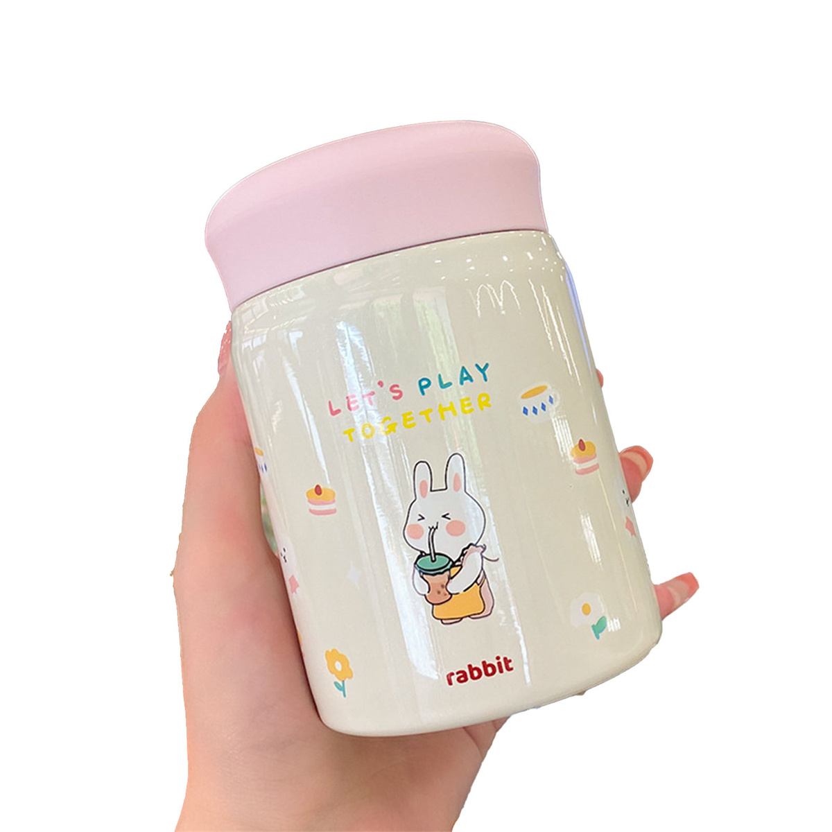 Eine Hand, die einen weißen, zylindrischen Becher mit Cartoon-Kaninchen und pinkem Deckel hält.
