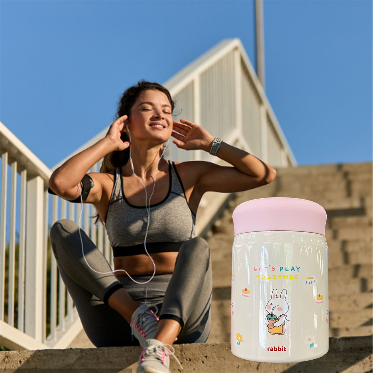 Eine Frau in Sportkleidung hört Musik. Ein rosa-deckeliger Becher mit Hasenmotiv steht daneben.
