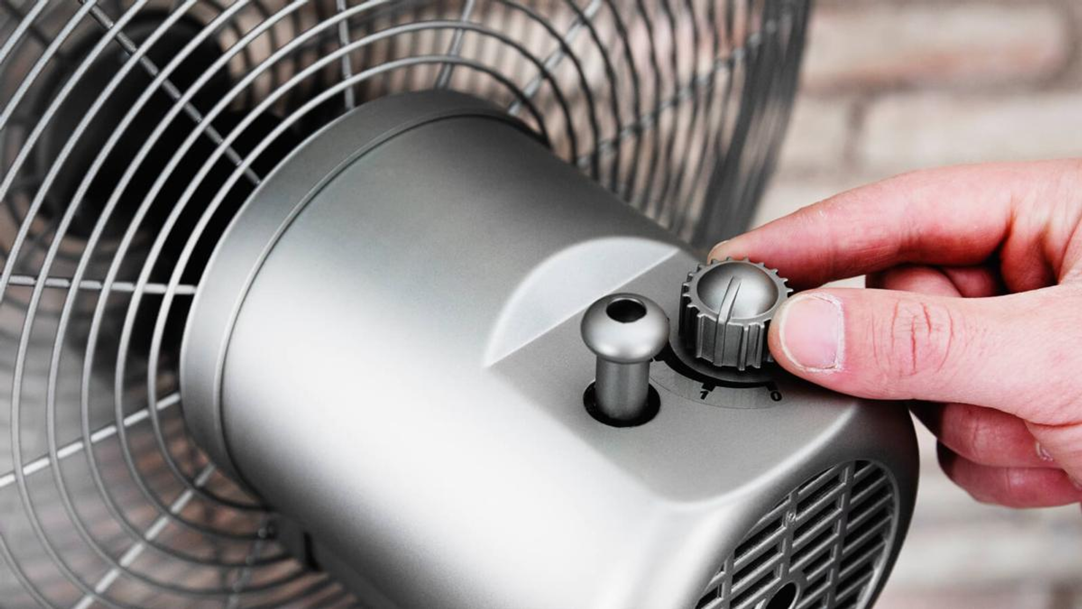 Una mano girando un dial en un ventilador eléctrico plateado, primer plano.
