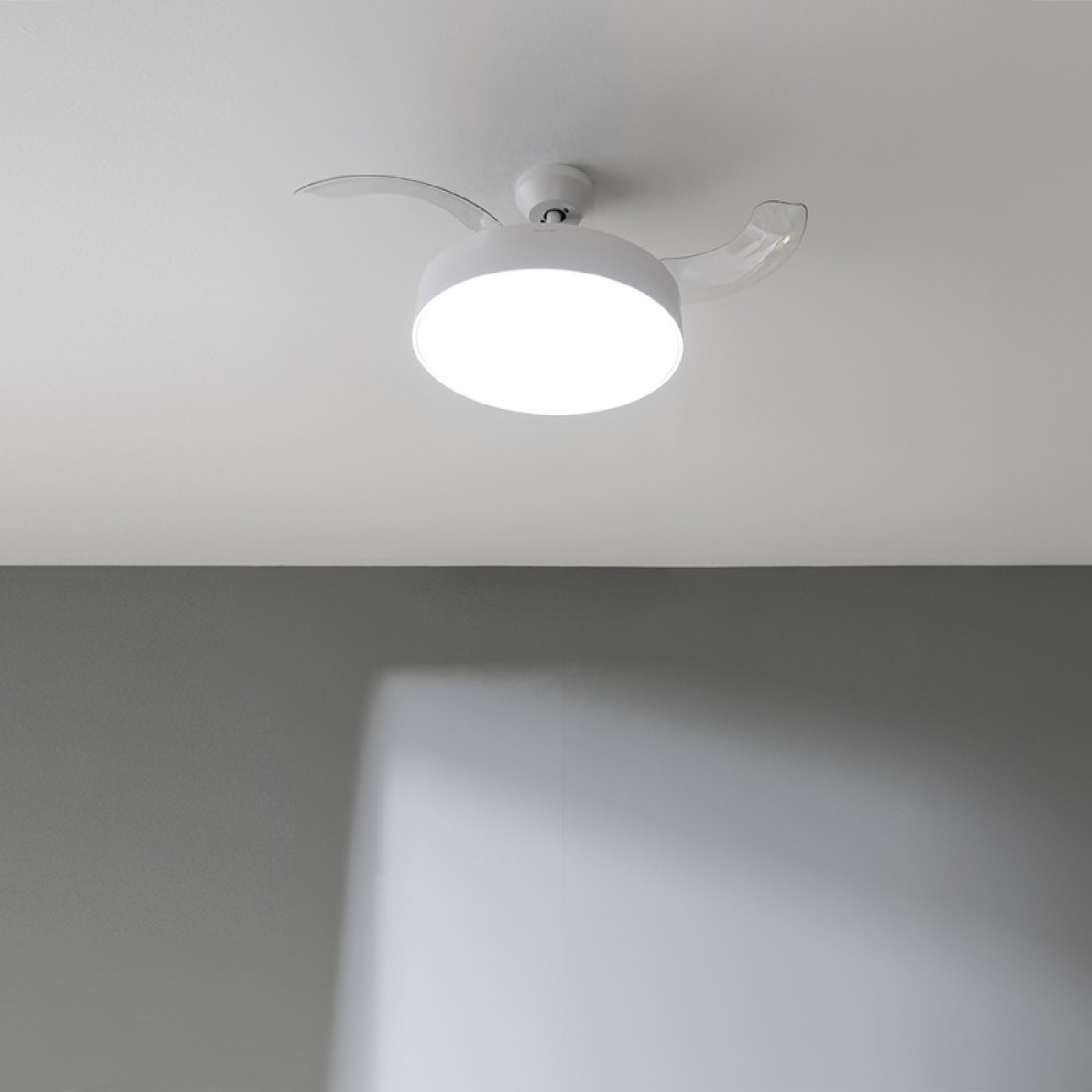 Un ventilatore da soffitto bianco con luce rotonda e due pale trasparenti.