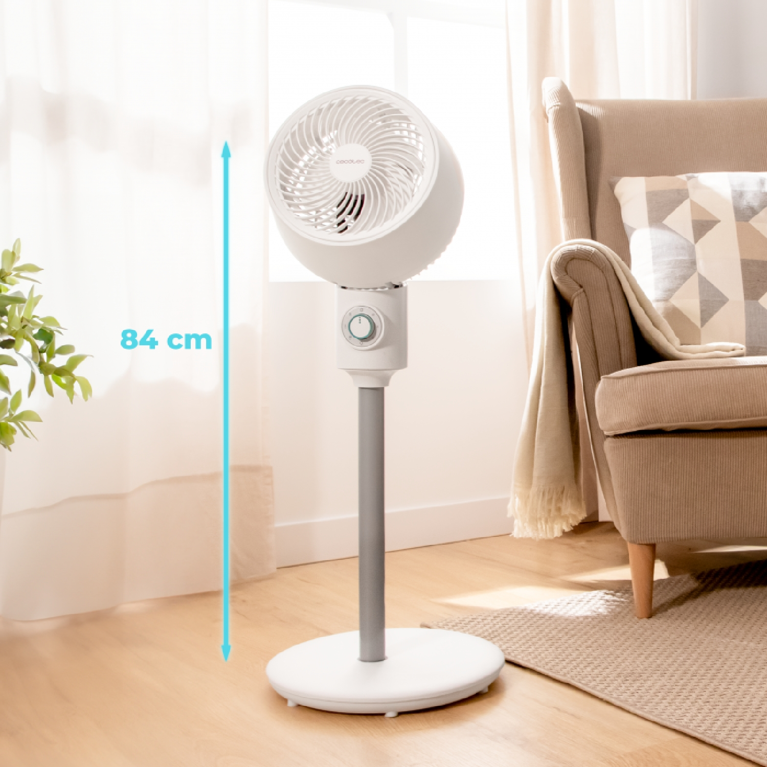 Ventilatore bianco con supporto grigio. Divano e finestra sullo sfondo.