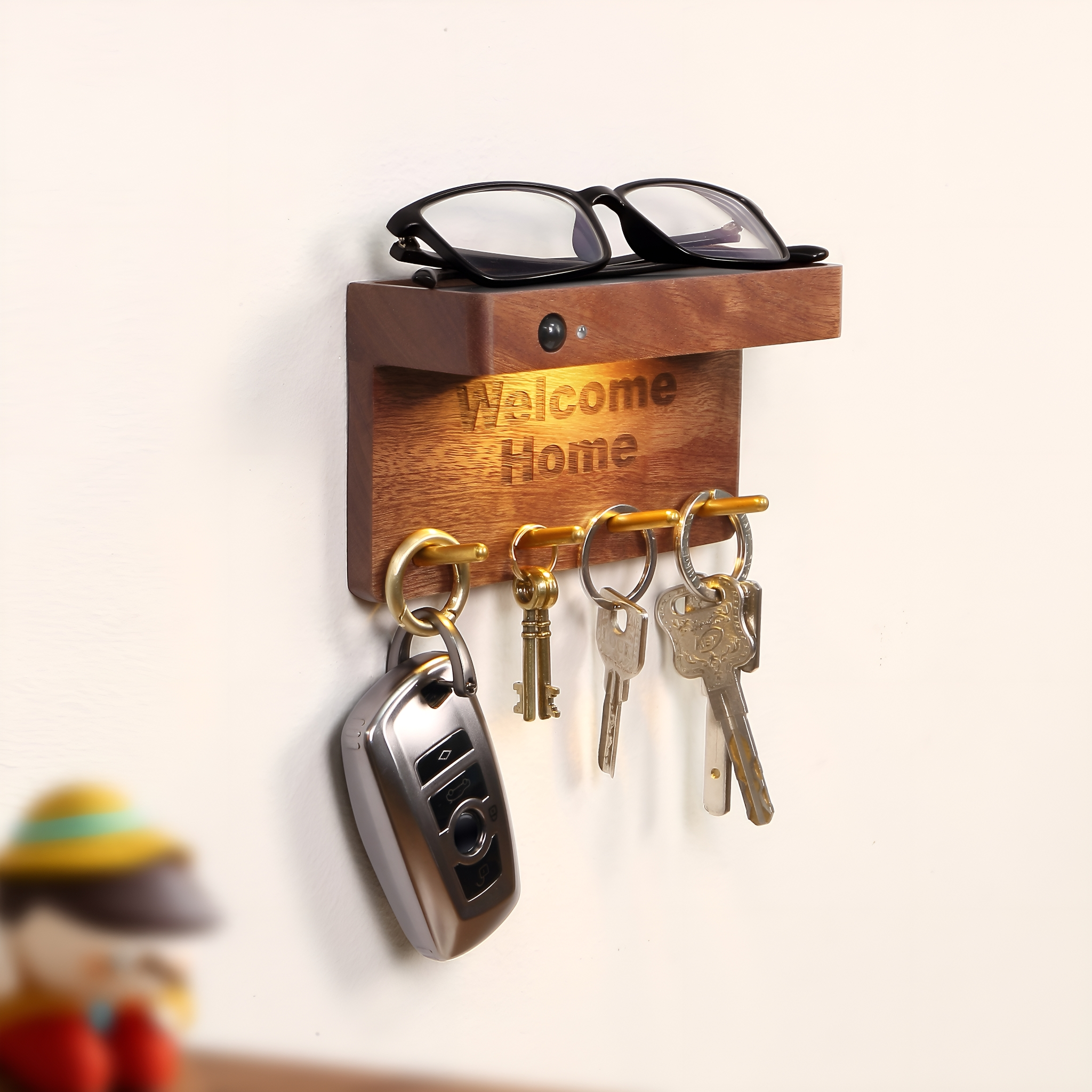 Schlüsselhalter aus Holz mit den Worten "Welcome Home" und Brille. Es hält Schlüssel und einen Autoschlüssel.