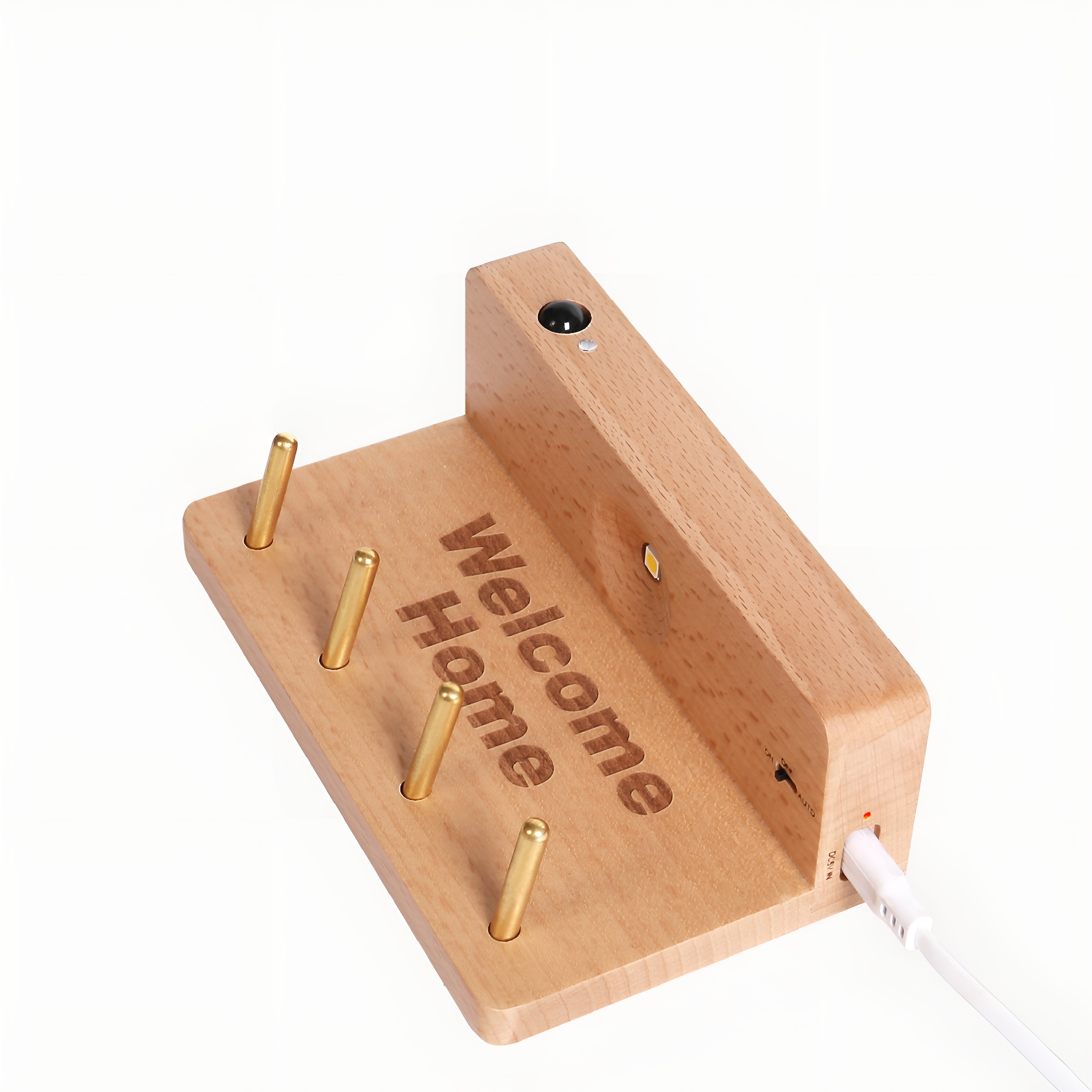 Hölzerner Schlüsselhalter mit Messingstiften und Gravur „Welcome Home“. Ein weißes Kabel ist eingesteckt. Weißer Hintergrund.