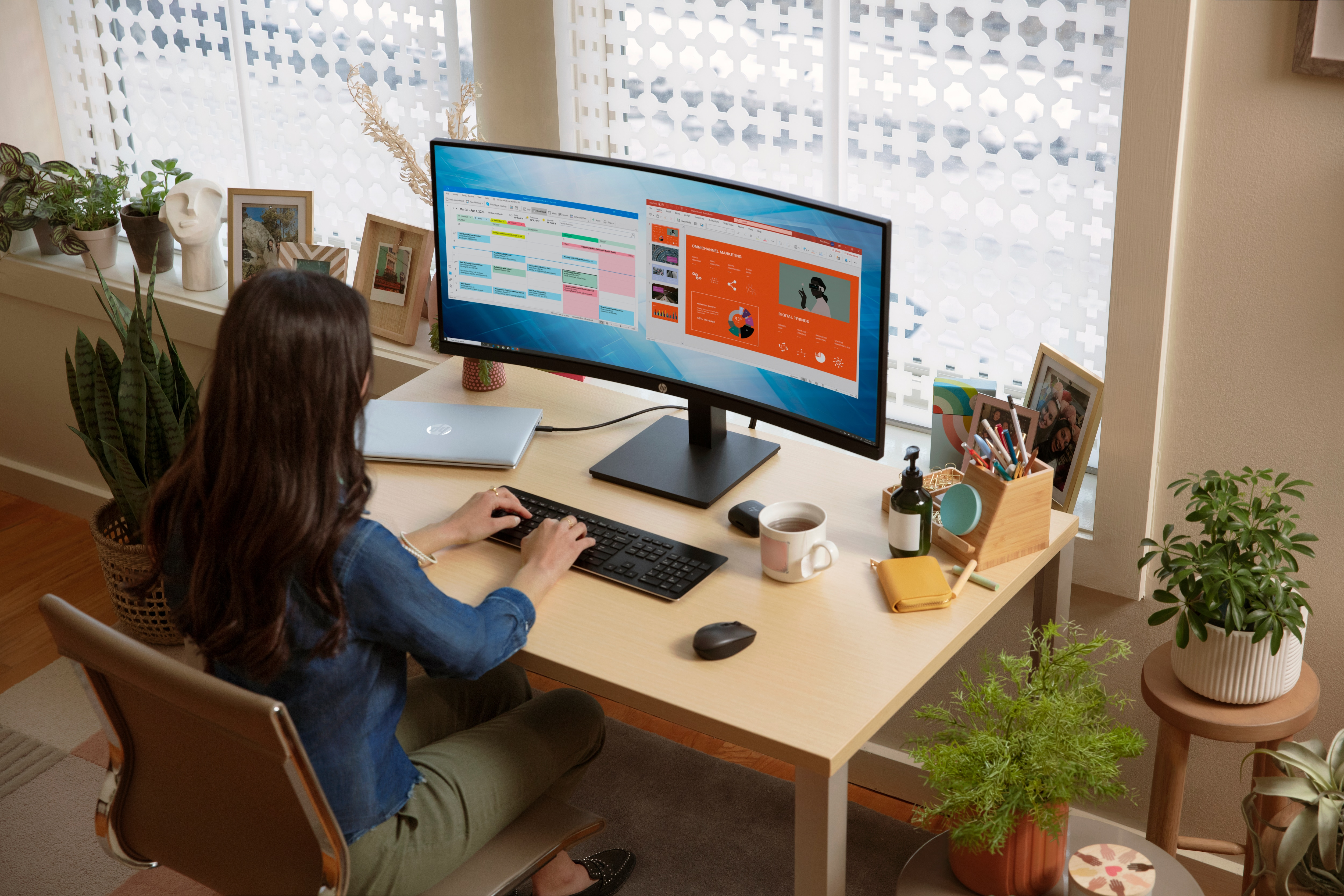 Una mujer sentada en un escritorio con un monitor HP. El monitor es curvo y muestra un calendario.