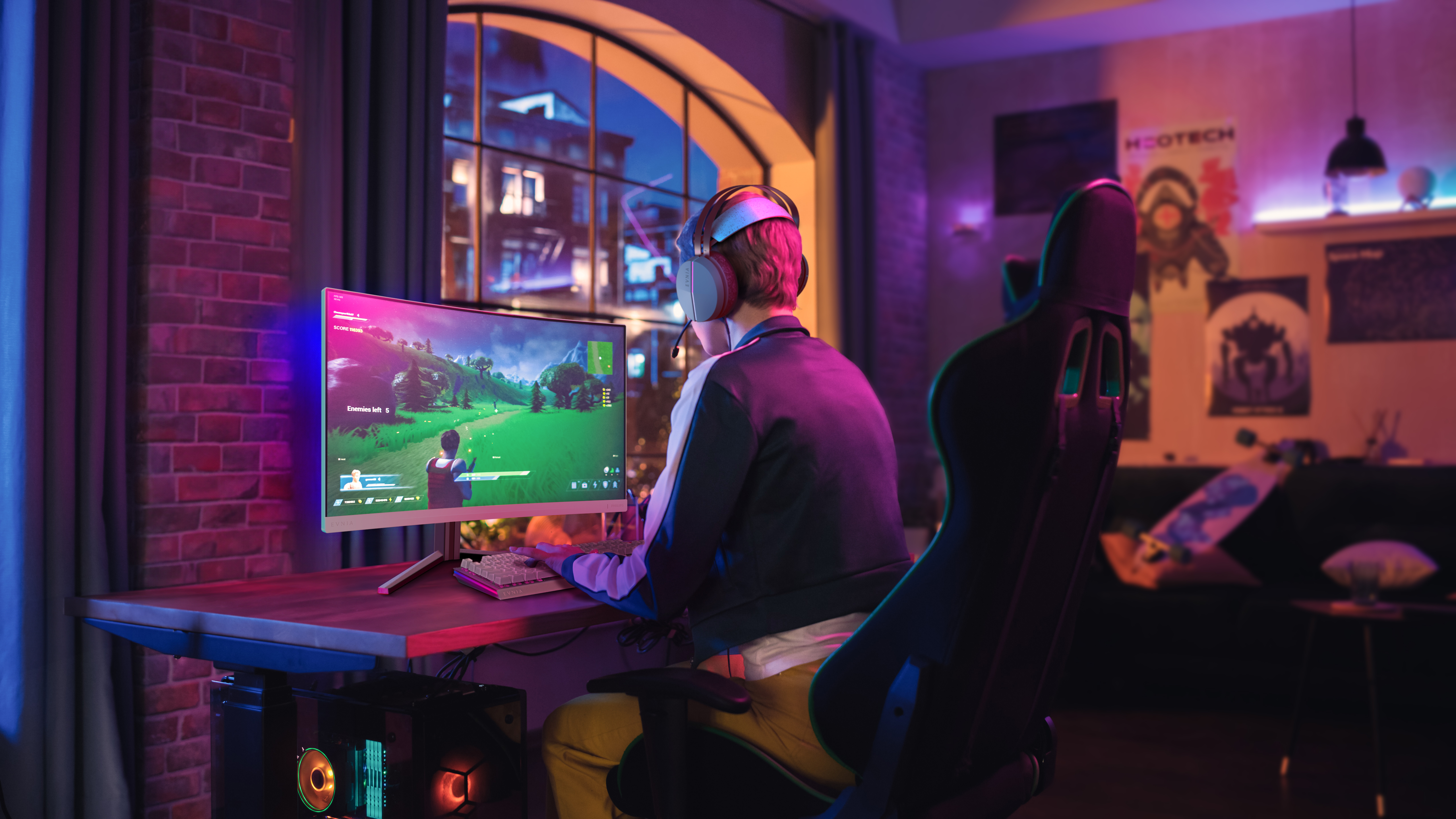Osoba w słuchawkach gra w pokoju oświetlonym kolorowymi światłami. Monitor na biurku.