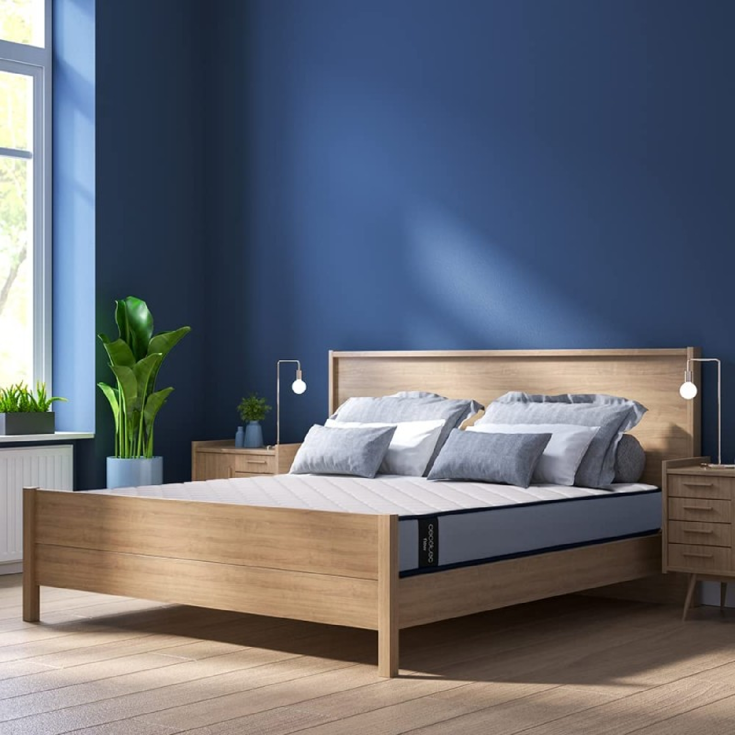 Escena de dormitorio con cama y pared azul. La cama tiene almohadas y un colchón gris. Dos mesitas de noche.