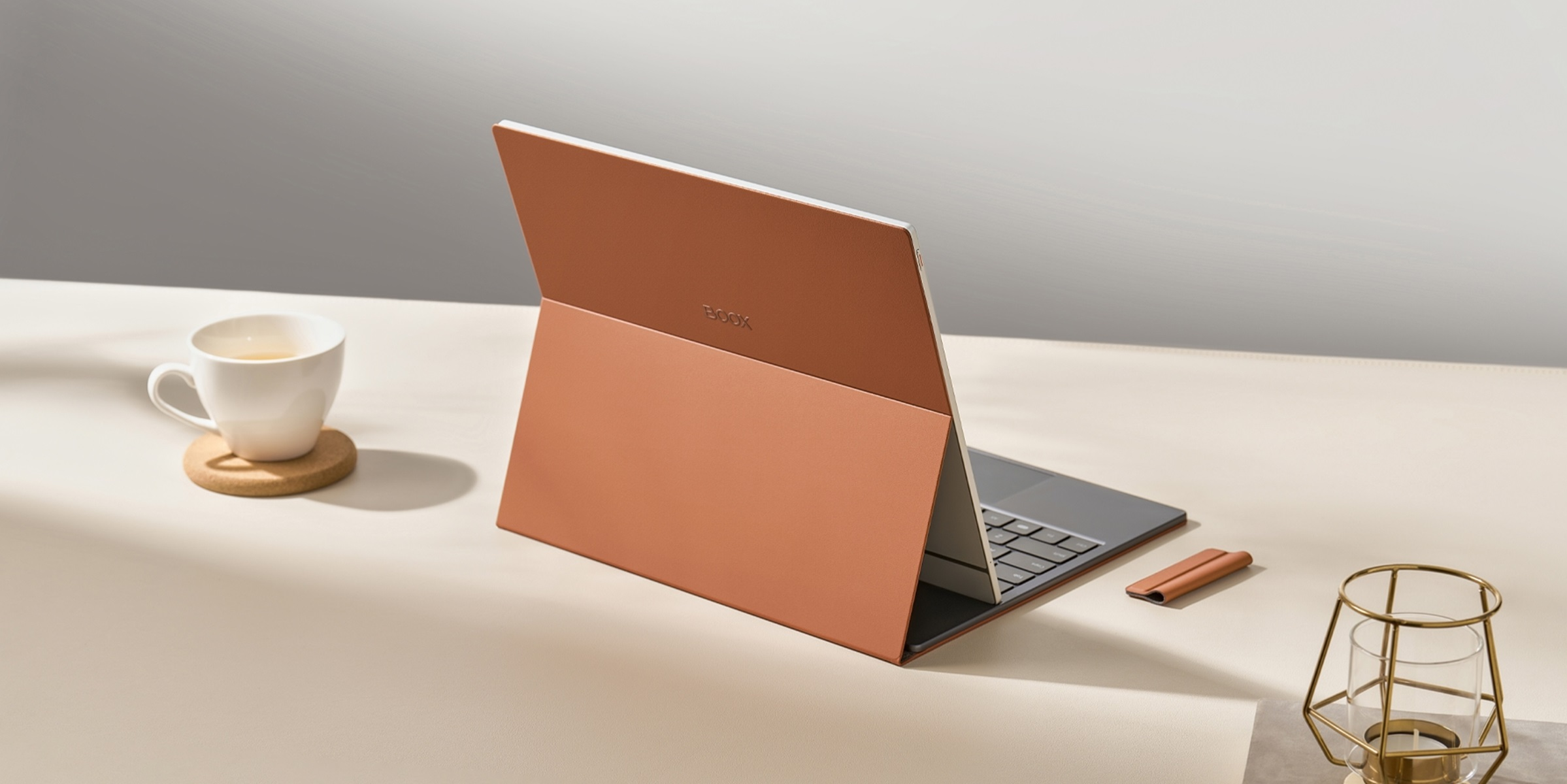 Laptop con copertina terracotta aperto su una scrivania con tazza, sottobicchiere e candeliere.