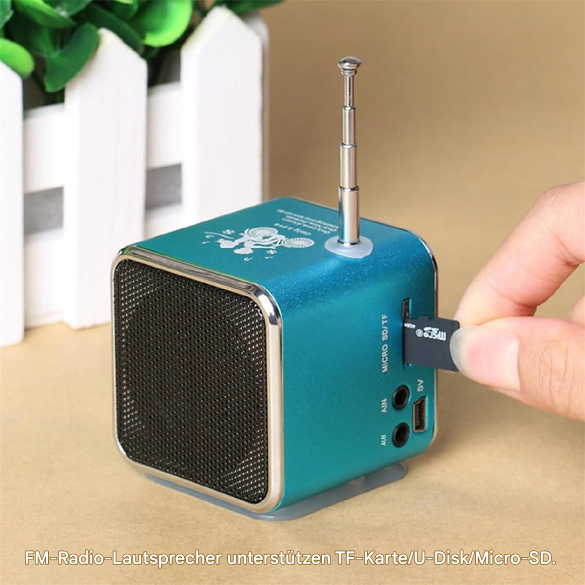 Ein türkisfarbener Mini-Lautsprecher mit Antenne, USB-Anschluss und einer Hand, die einen USB-Stick einsteckt.