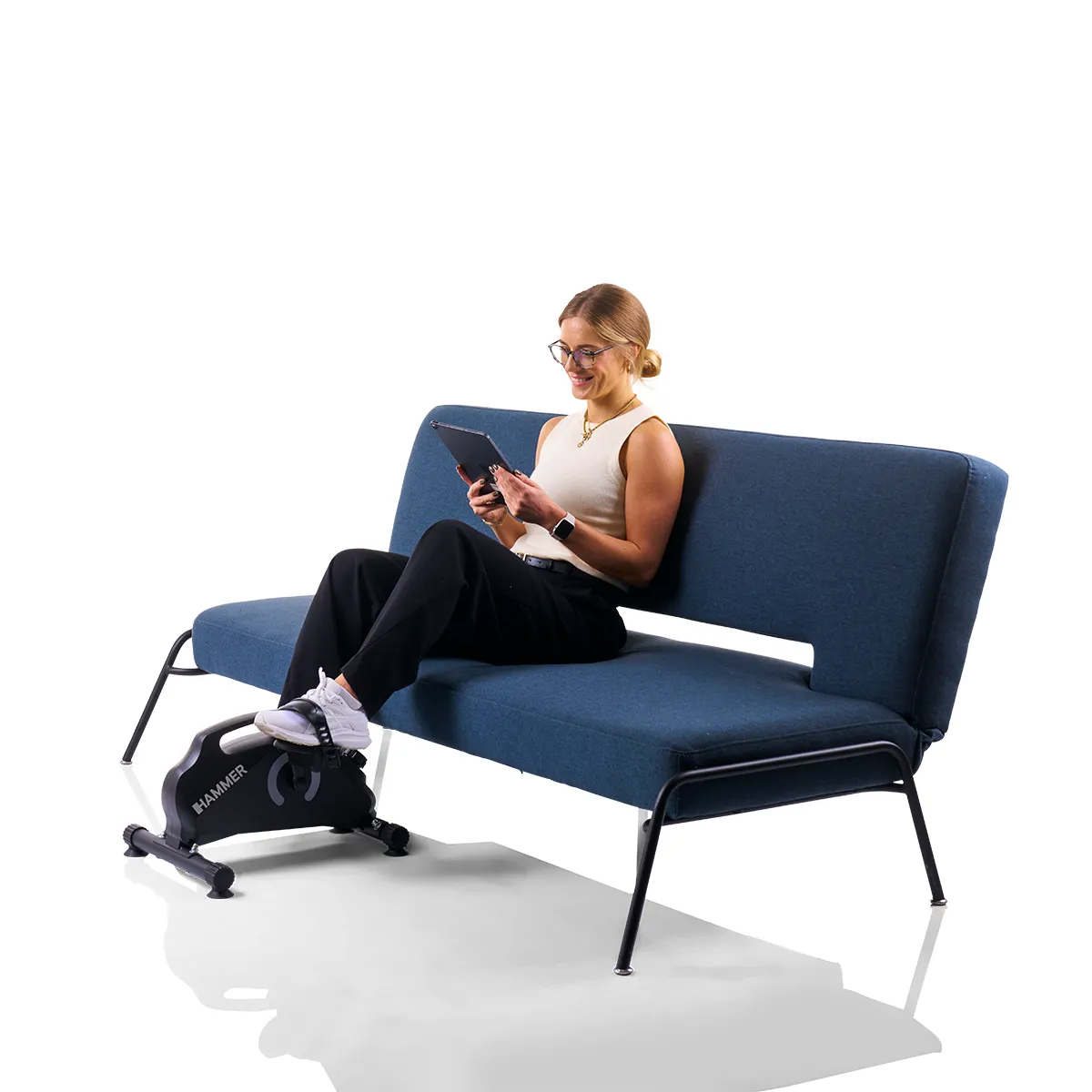 Frau auf blauem Sofa mit Tablet, mit Heimtrainer. Weißer Hintergrund, Tageslicht.