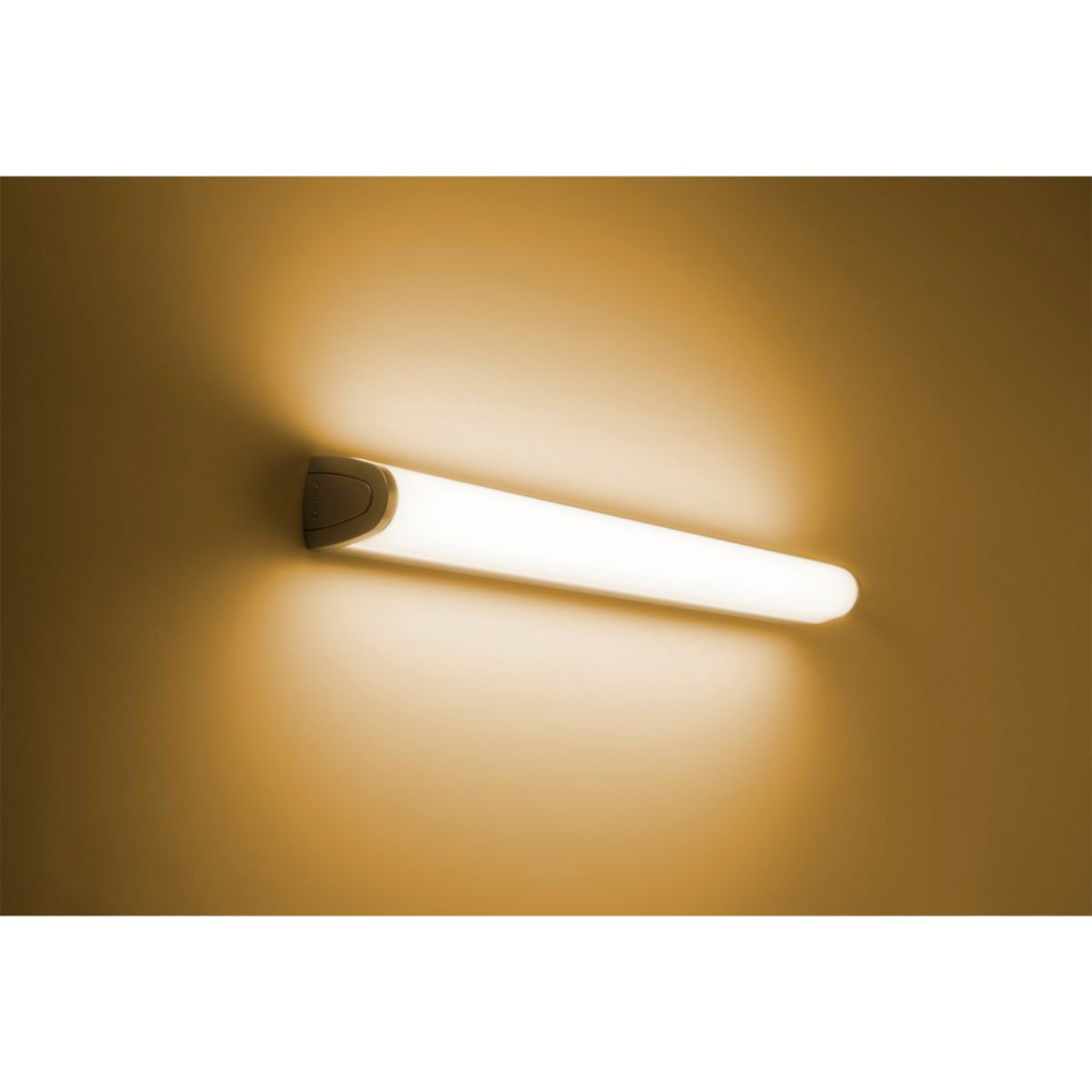 Eine weiße, lange, röhrenförmige Leuchte ist an einer hellbraunen Wand befestigt und wirft ein warmes Licht.