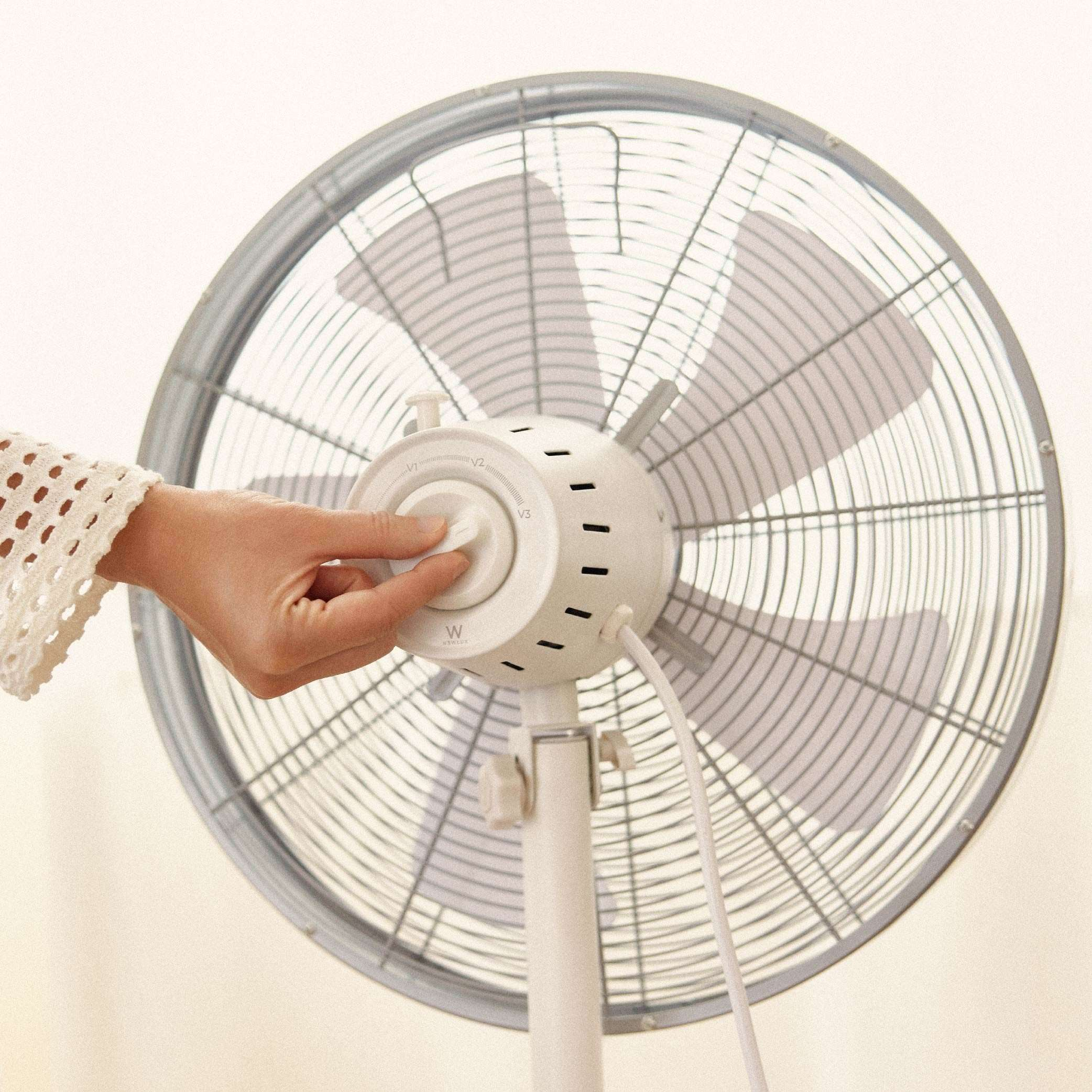 Mano ajustando el mando de velocidad de un ventilador blanco. Fondo blanco.