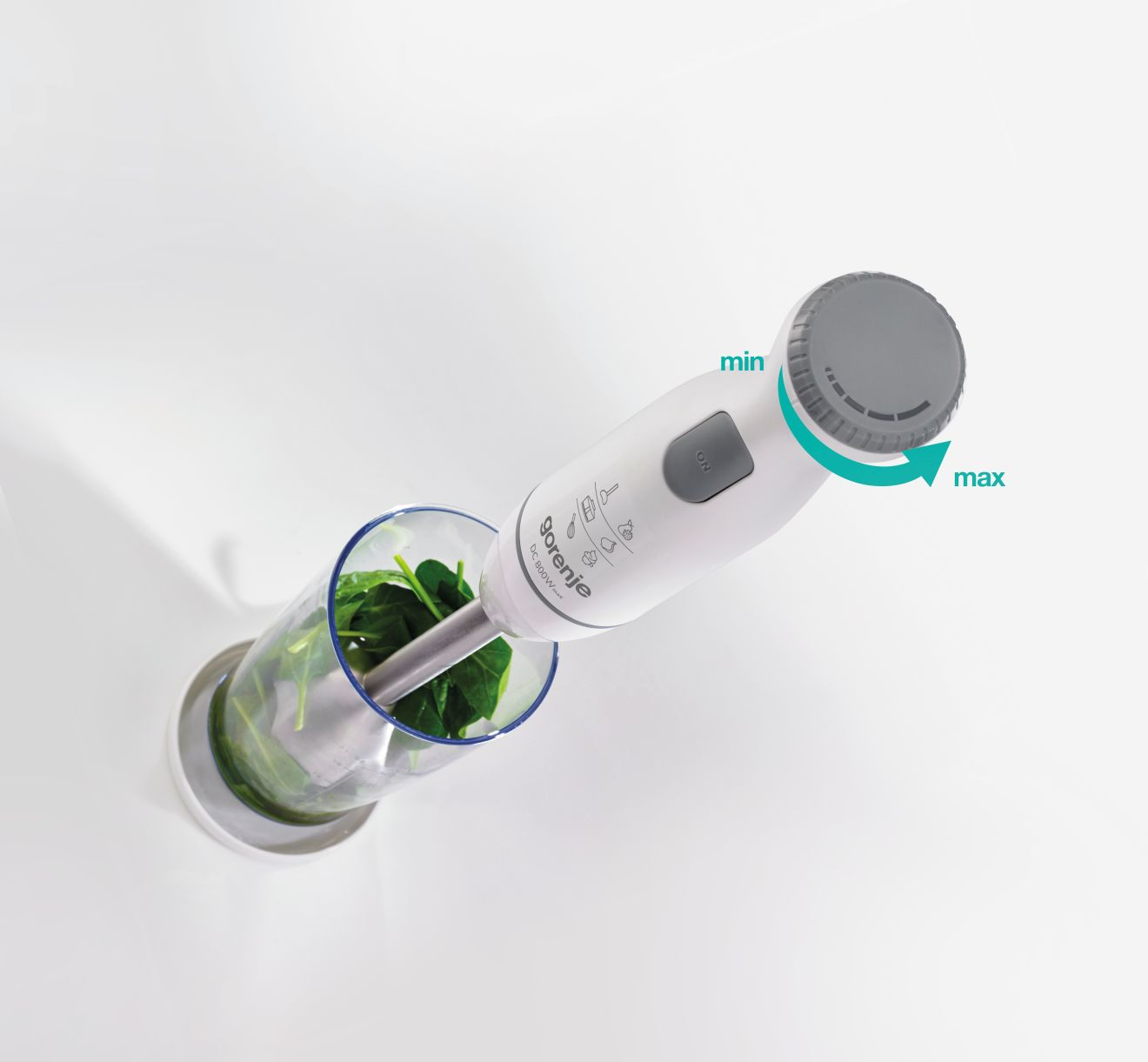 Een staafmixer die spinazie in een glas mengt, met min- en max-bediening.