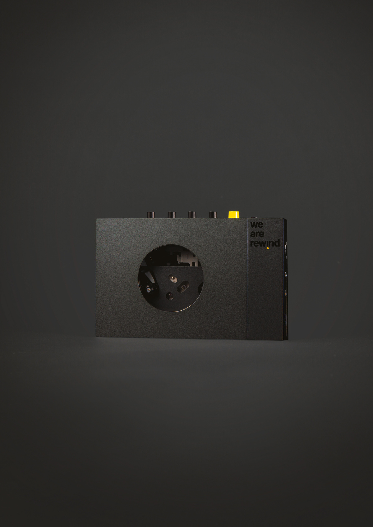 Lecteur de cassettes noir avec boutons et texte 'we are rewind'. Fond gris foncé.