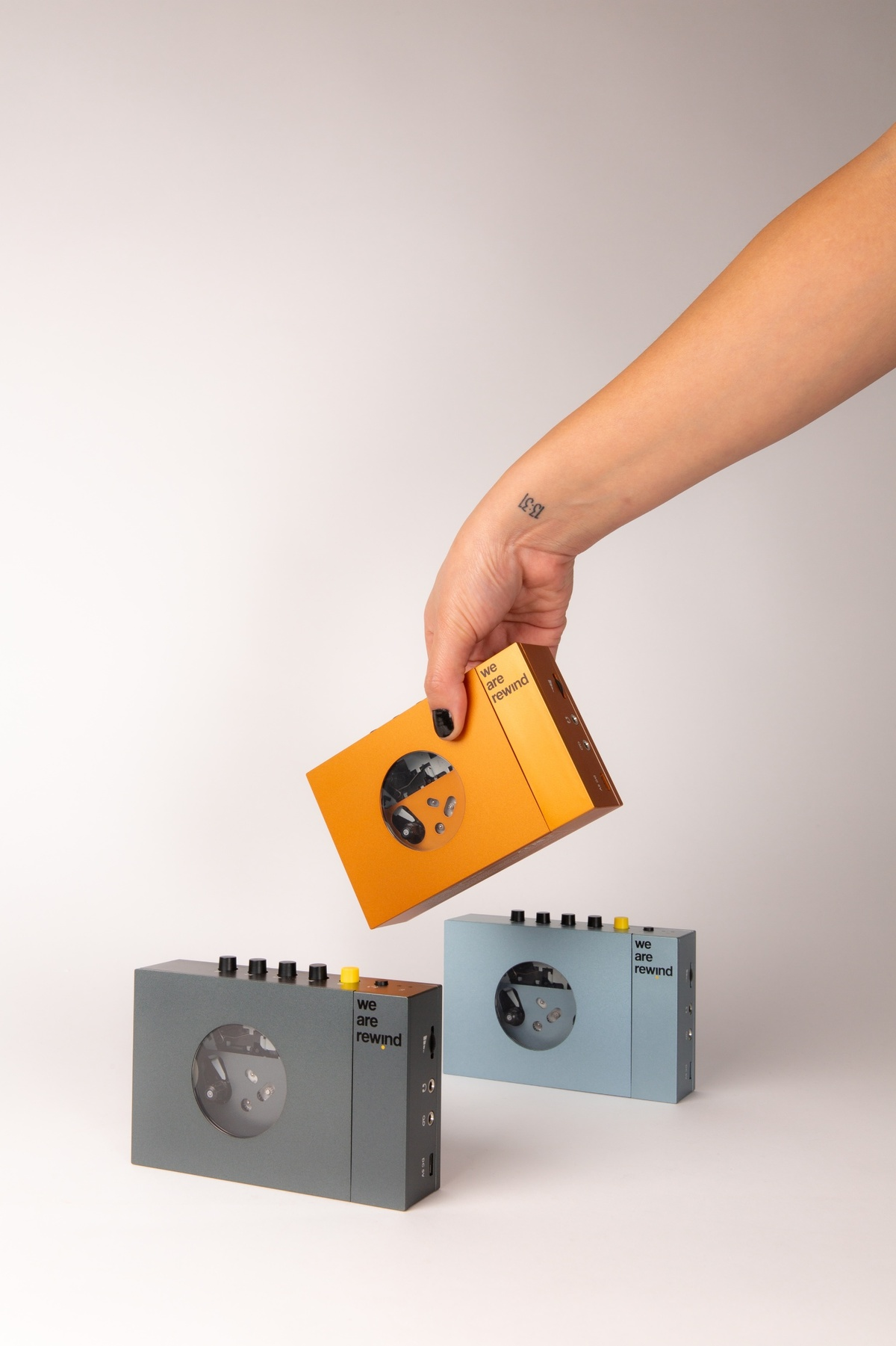Trois lecteurs de cassettes rétro, un tenu par une main, de différentes couleurs sur fond blanc.