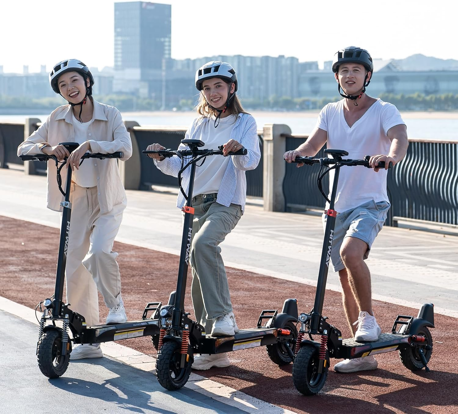 Tres personas en patinetes en un camino pavimentado. Llevan cascos y se dirigen hacia el espectador.