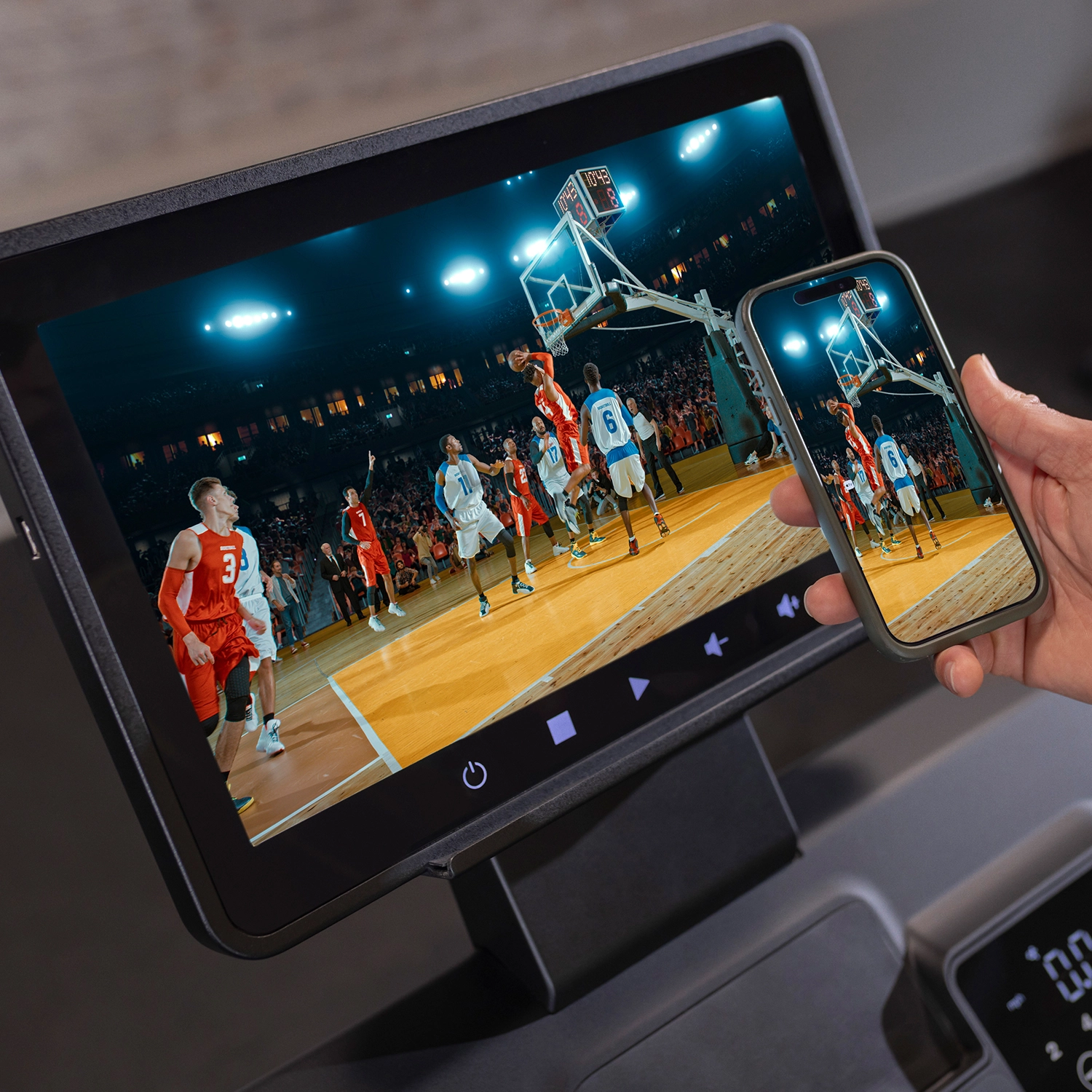 Ein Bildschirm zeigt ein Basketballspiel. Ein Telefon zeigt dasselbe Spiel. Eine Hand hält das Telefon.